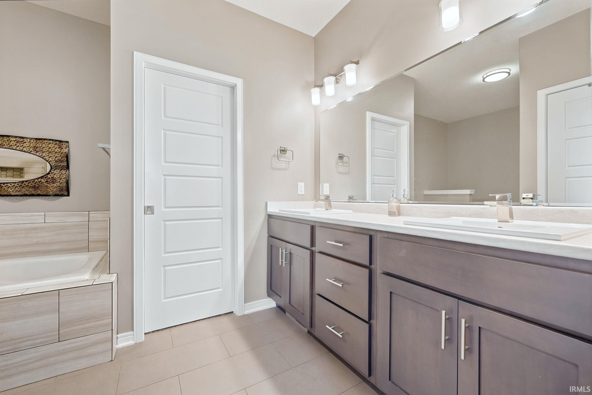 Bathroom featuring a double vanity with undermount sinks, a large wall-mounted mirror, and a tiled soaking tub