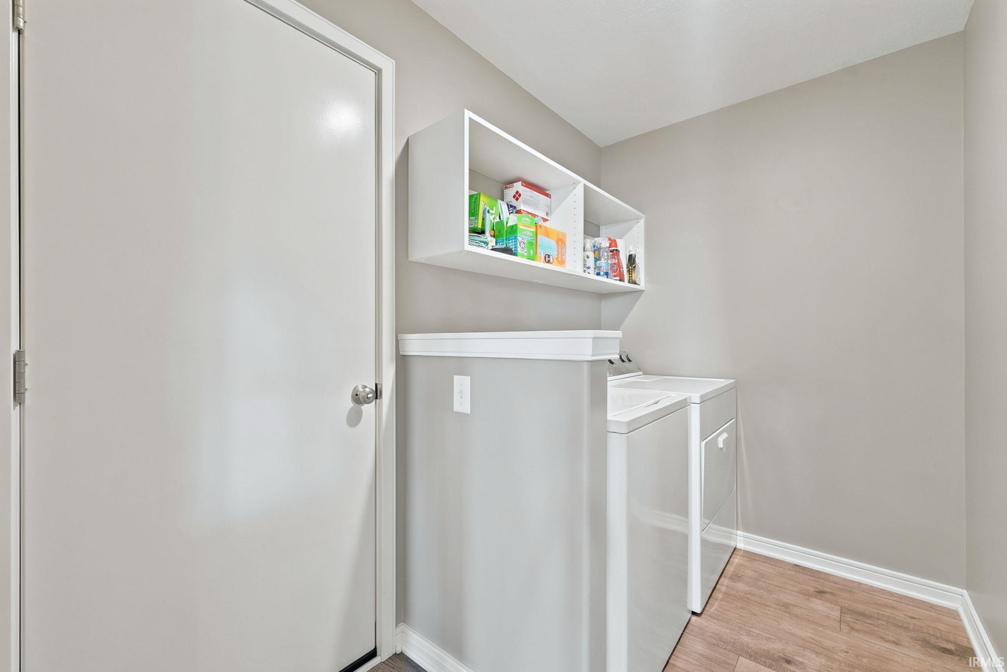 Dedicated laundry space featuring wood-finish flooring, light grey painted walls, white baseboards, and built-in white shelving