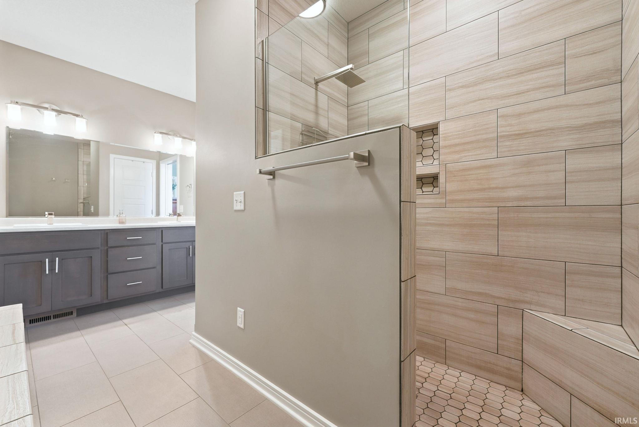 Walk-in shower featuring large format tile walls, hexagonal floor tiles, a built-in bench, and recessed shelving