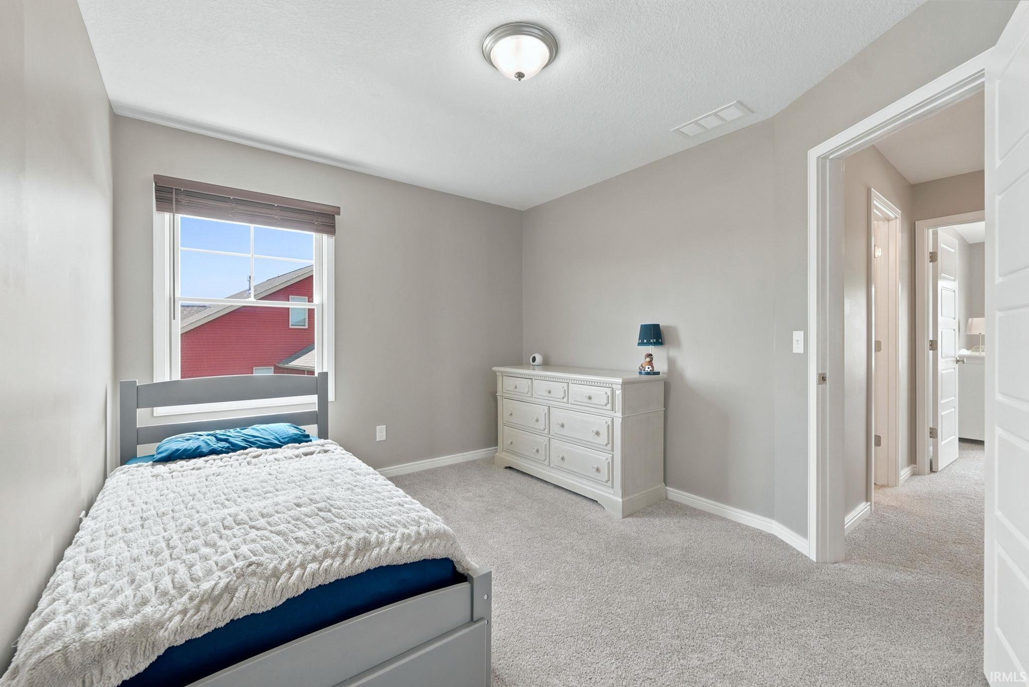 Interior room featuring light gray wall paint, a single window with blinds, a ceiling-mounted light fixture, and light gray carpeting