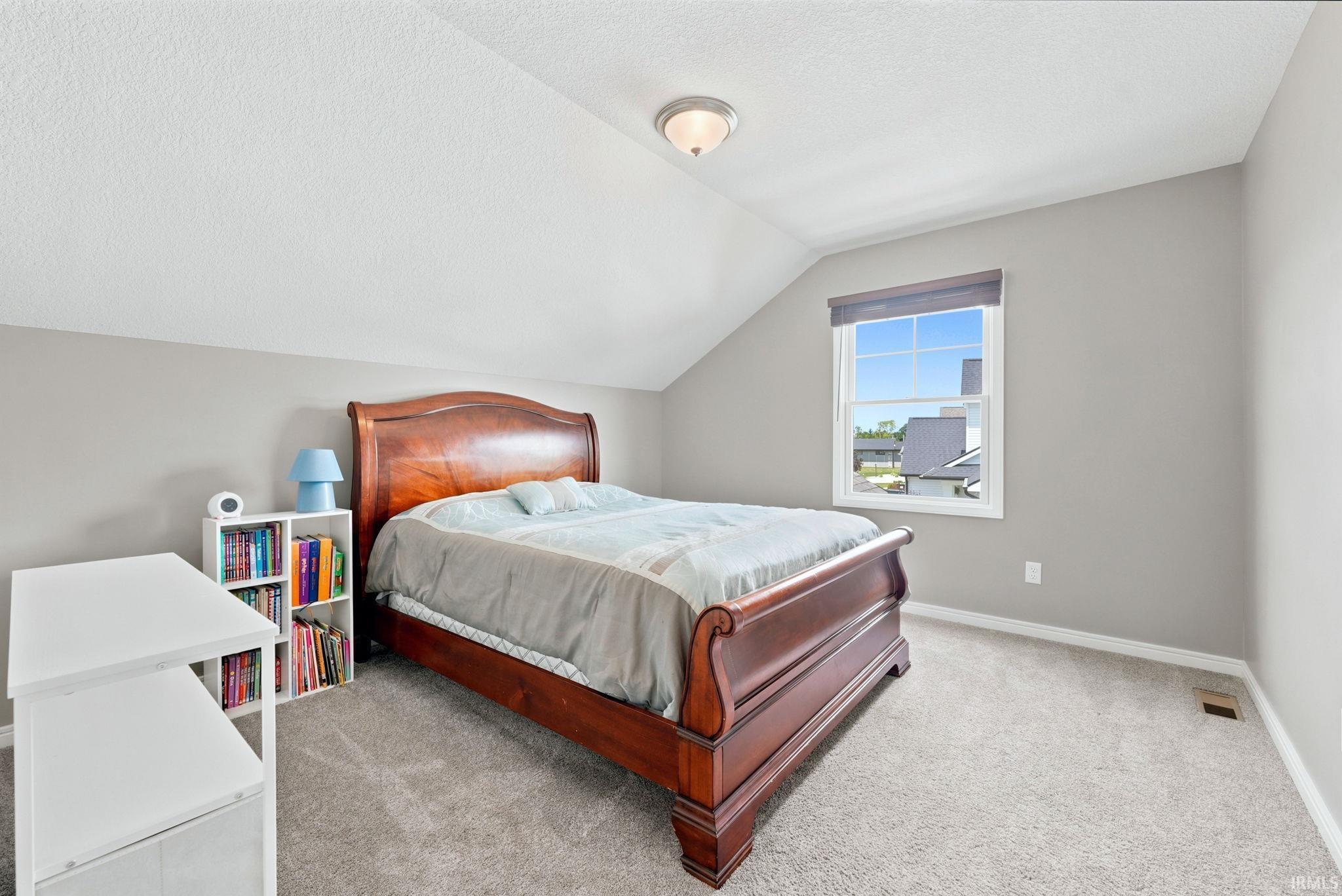 Carpeted room featuring a single window with a roller shade, sloped ceiling design, and a flush-mount light fixture