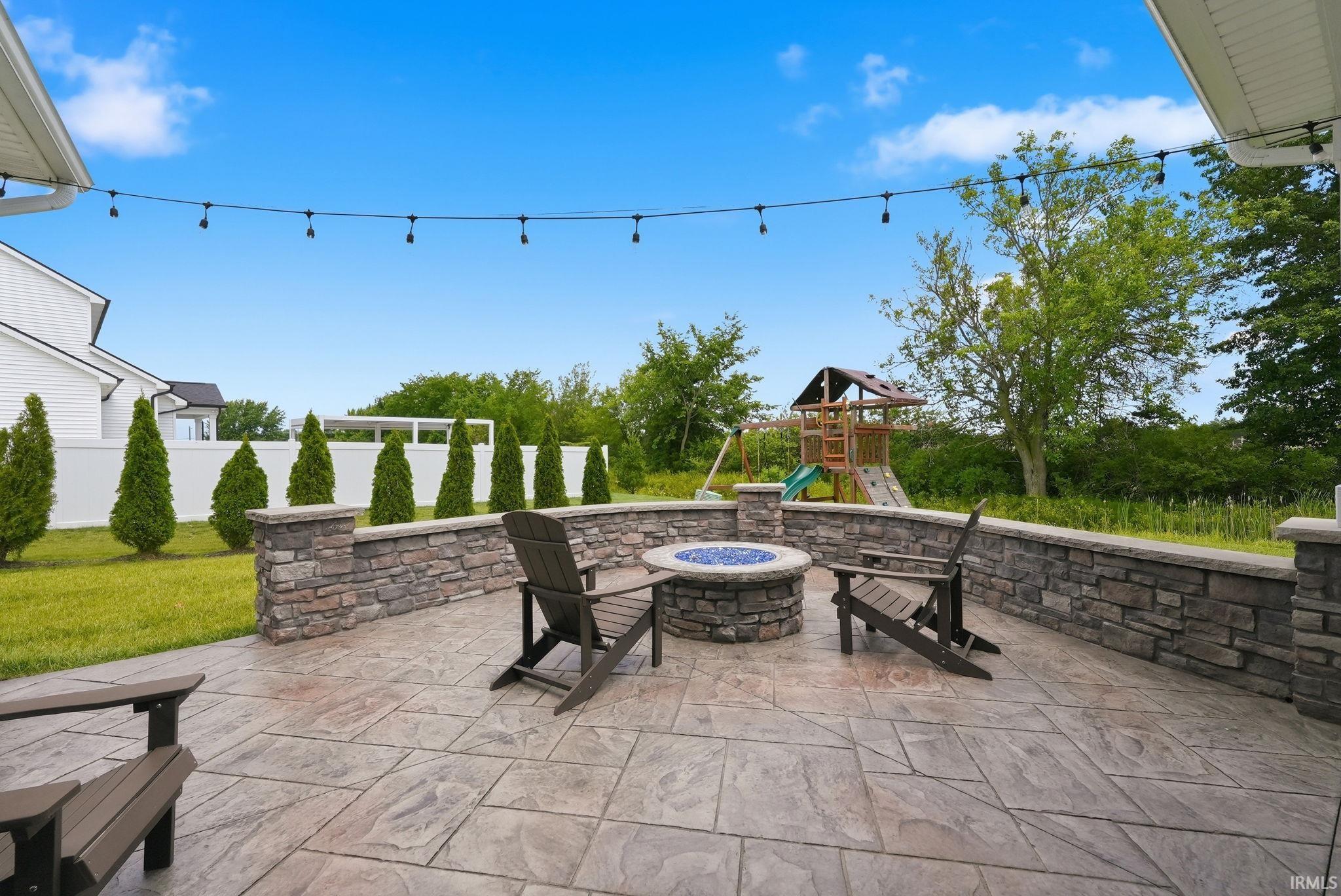 Expansive backyard patio featuring stamped concrete, a built-in stone fire pit, and stone retaining walls