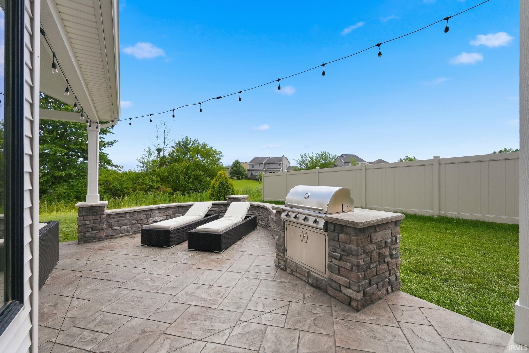 Stamped concrete patio featuring an outdoor kitchen with built-in grill, stone veneer accents, and string lighting under a covered porch