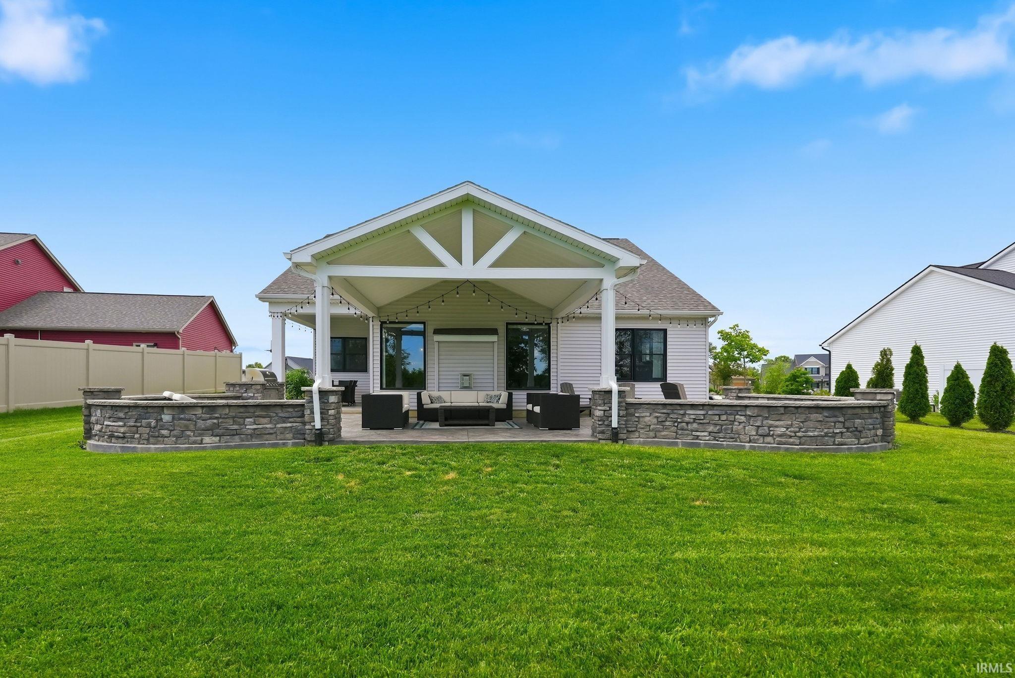 Expansive lawn featuring a covered patio, stone retaining walls, and a built-in fire pit