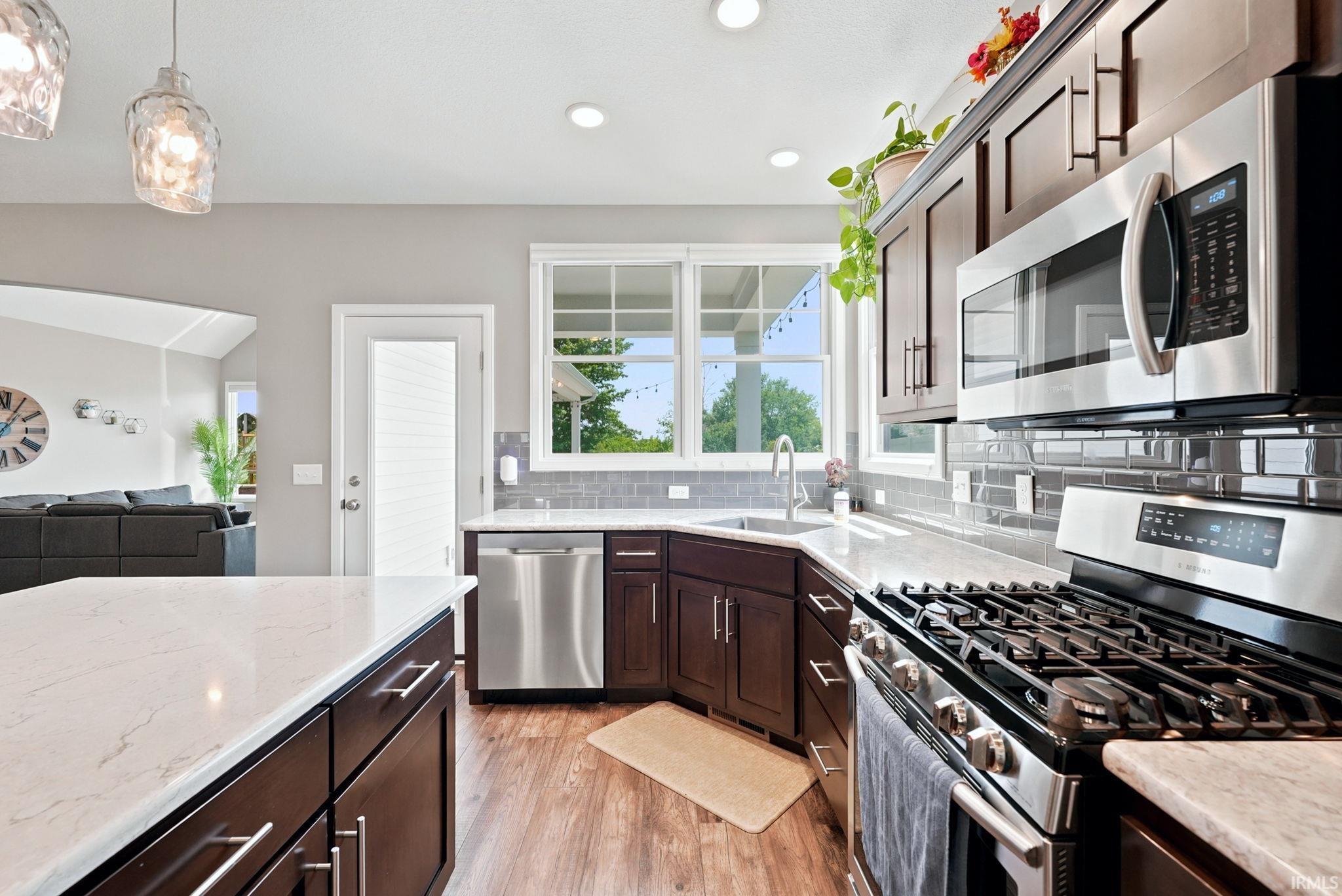 Modern kitchen featuring a gas range, stainless steel appliances, dark wood-finish cabinetry, light-toned countertops, and a subway tile backsplash