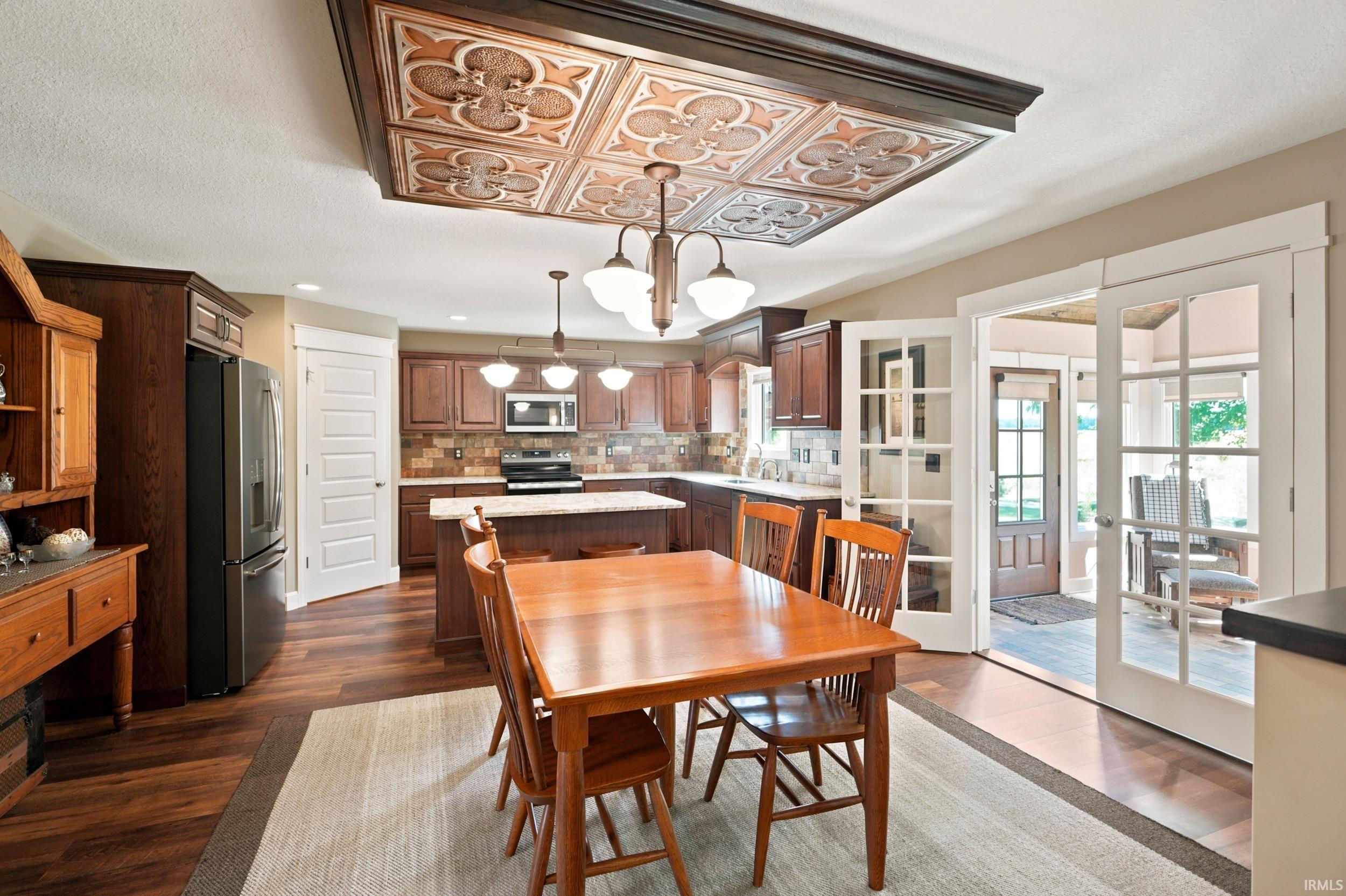 Kitchen and dining area featuring a decorative ceiling panel, dark wood-finish flooring, white paneled interior doors, and a kitchen island with seating
