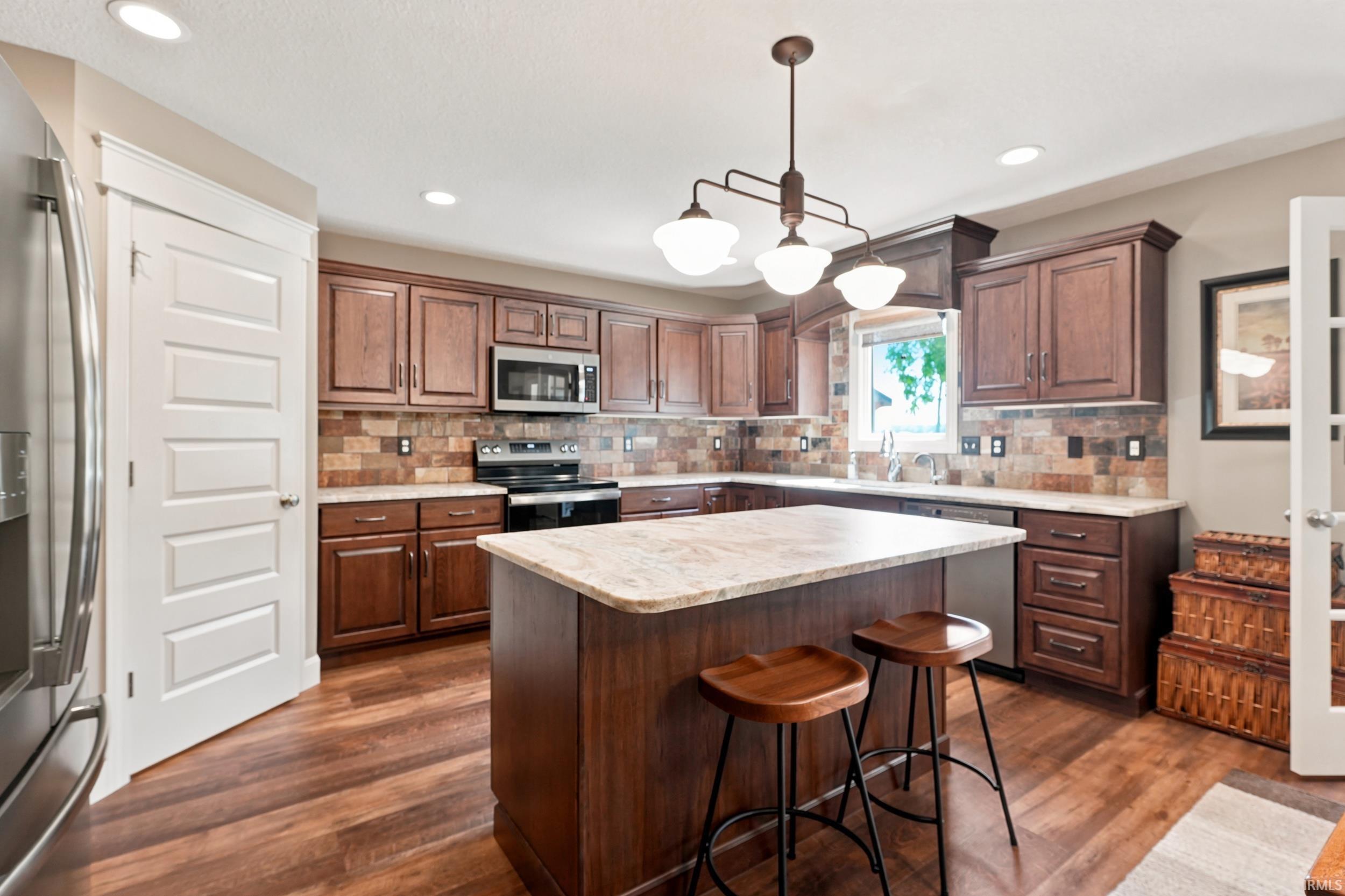 Kitchen featuring wood-finish flooring, dark wood cabinetry, a light-toned countertop, a tile backsplash, and recessed lighting