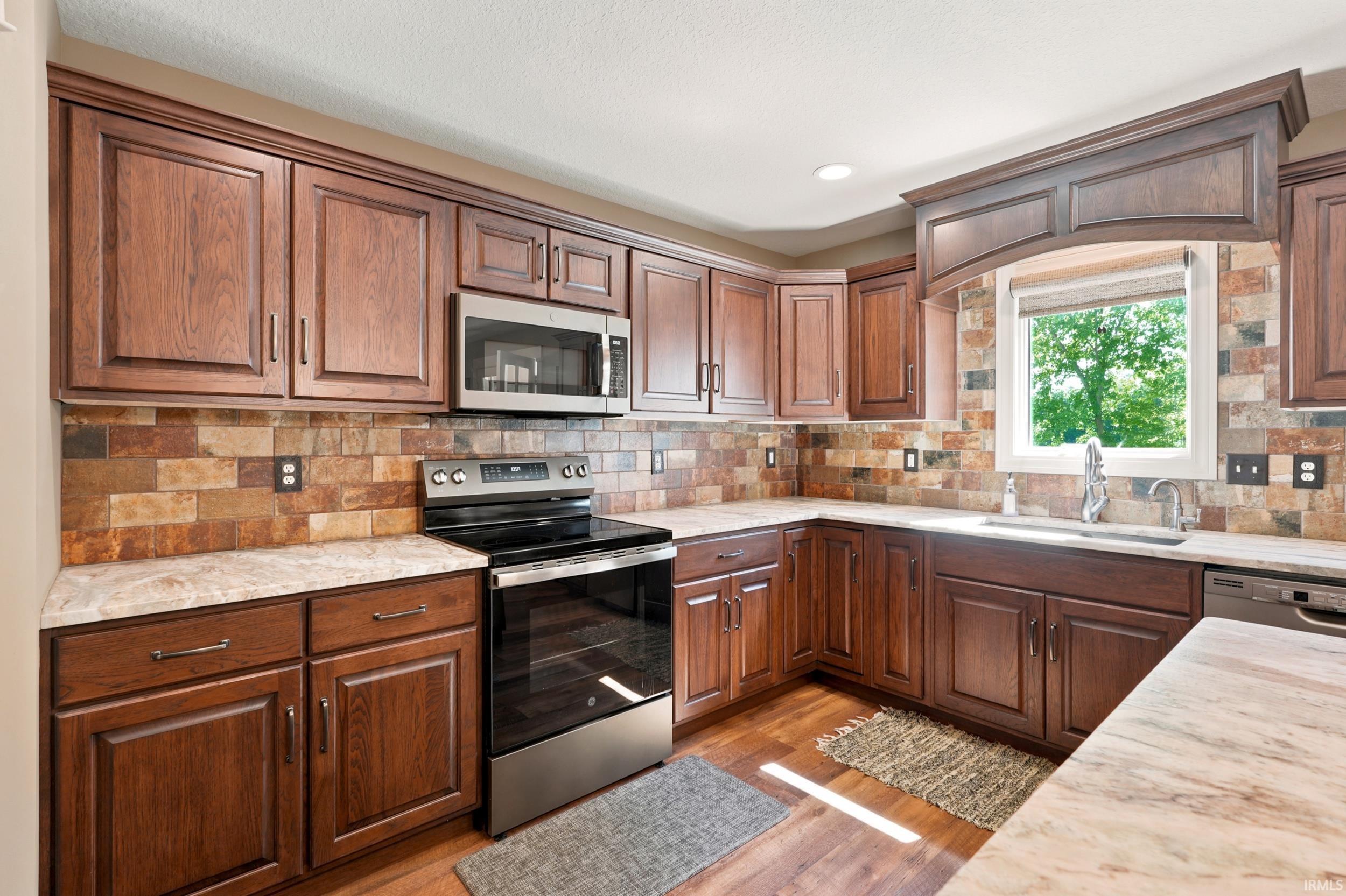 Kitchen featuring wood-finish cabinetry, stainless steel appliances, stone backsplash, and light-toned countertops