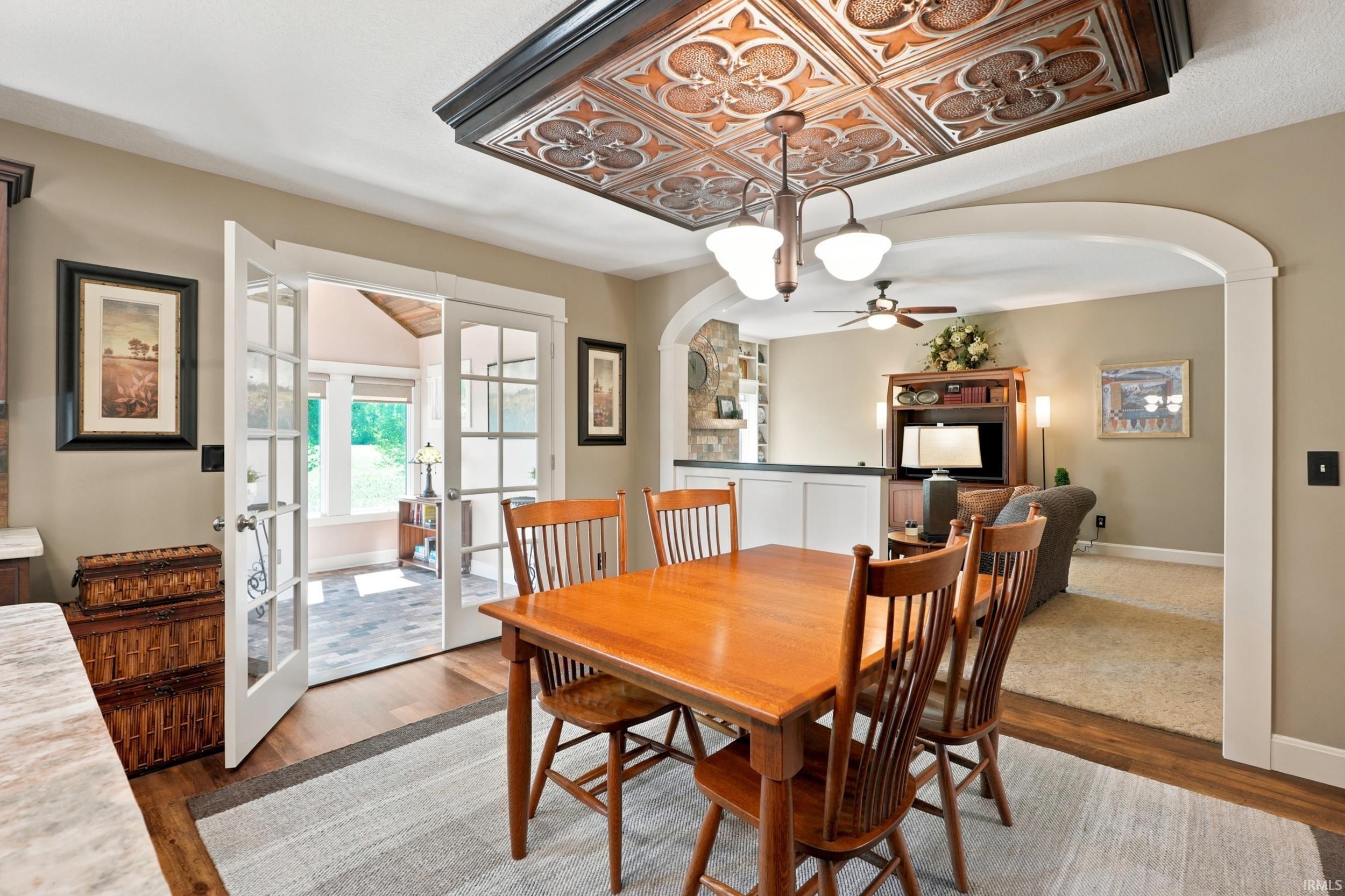 Dining area featuring a decorative metal ceiling panel with a chandelier, wood-finish flooring, and a large arched doorway