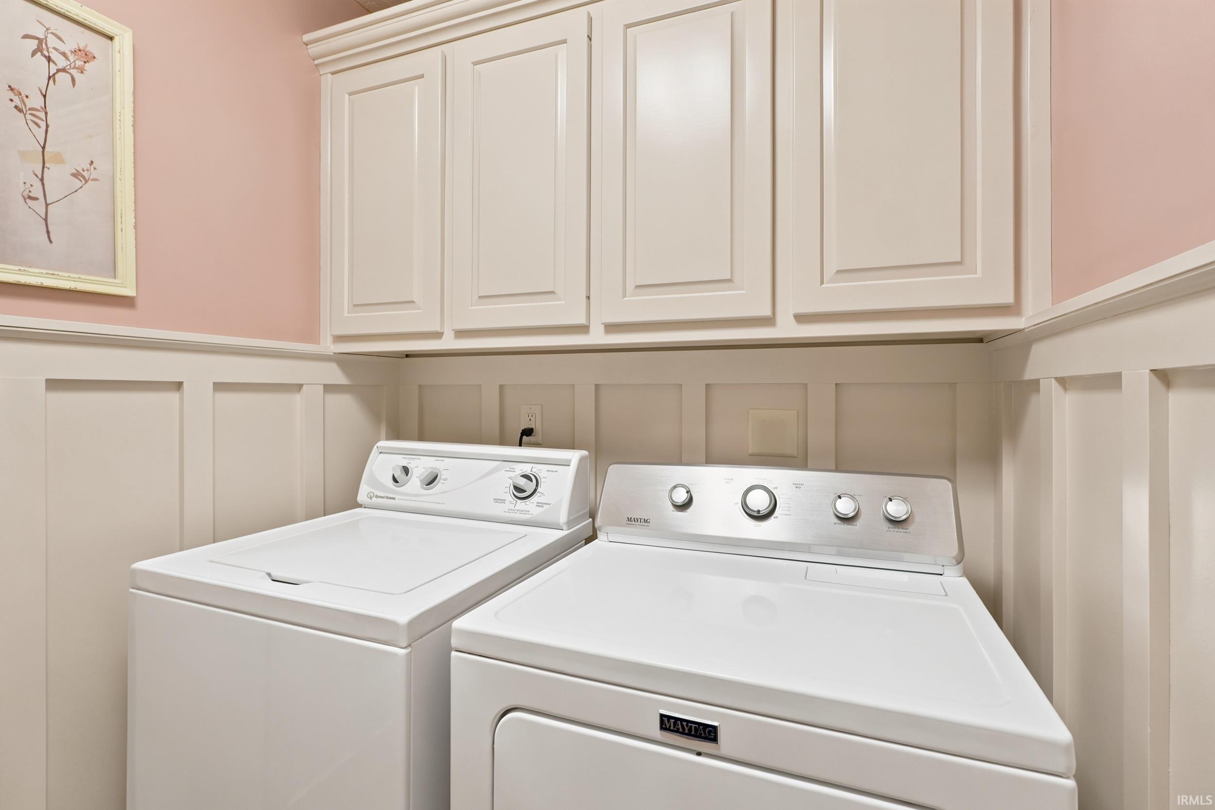 Laundry area featuring upper cabinetry, wainscoting, and a light pink wall finish