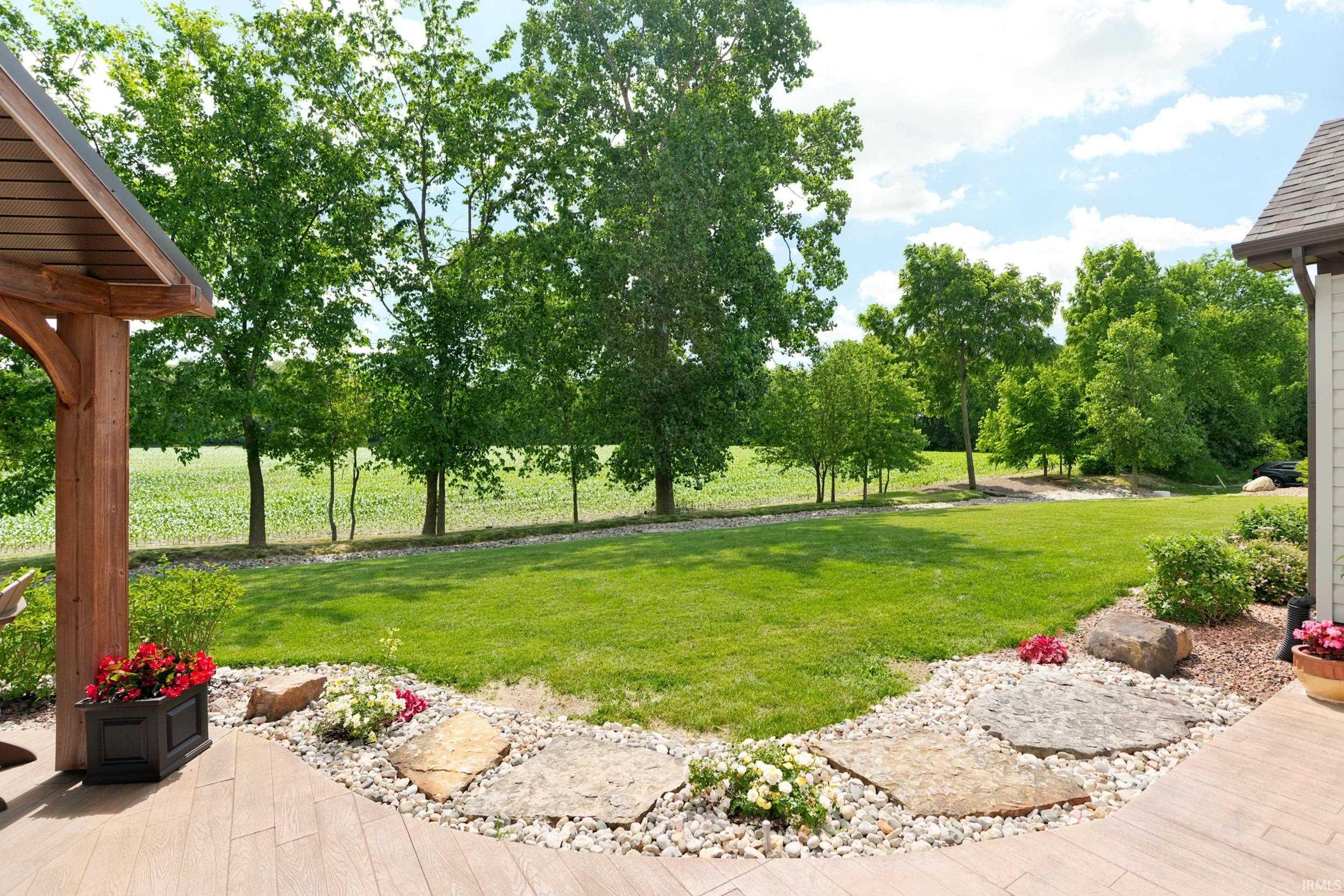 Expansive green space featuring lush lawn, mature trees, and a landscaped edge with stepping stones and decorative rock