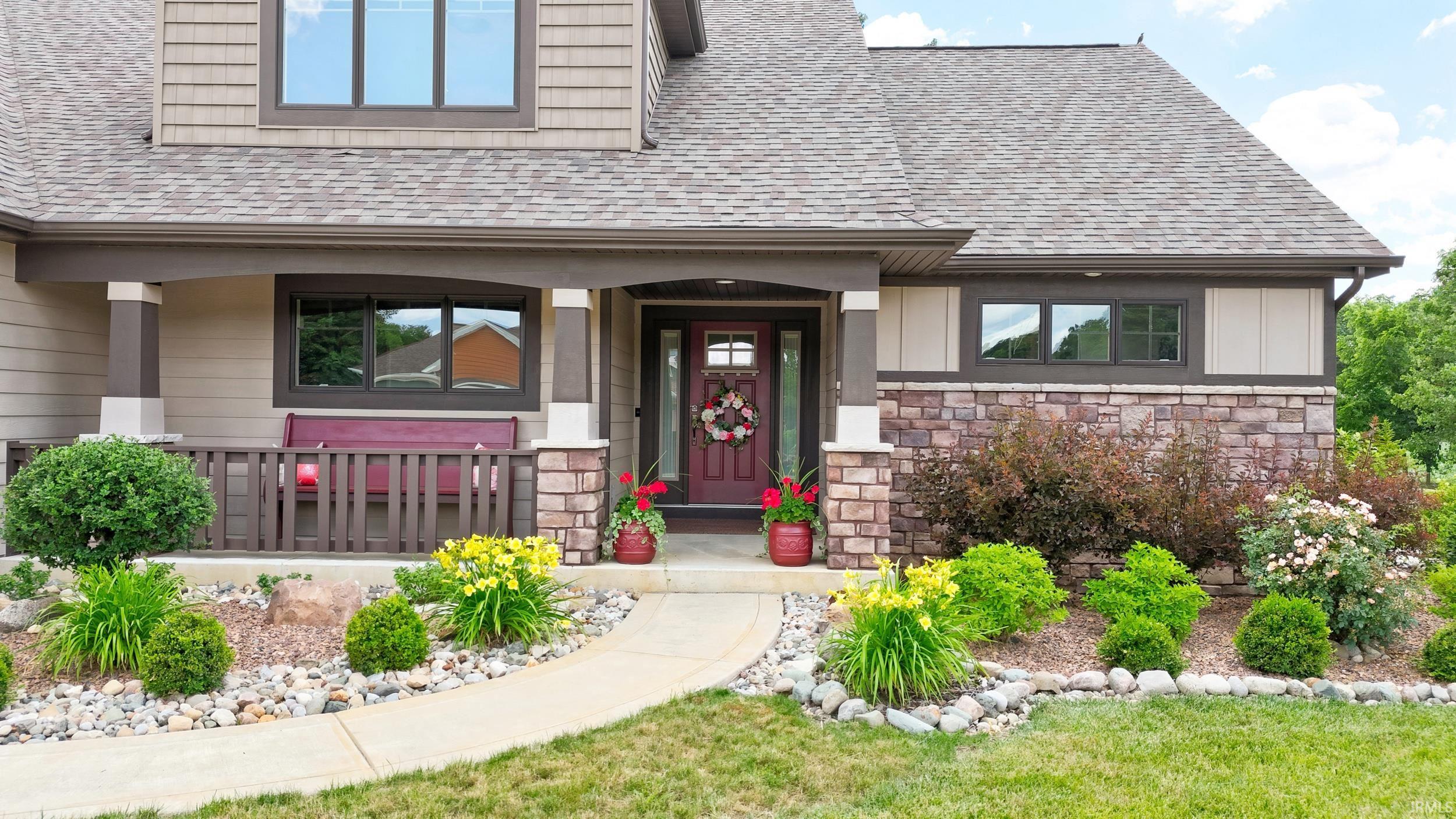 Inviting property entrance featuring a covered porch with decorative columns, stone veneer accents, and a concrete walkway