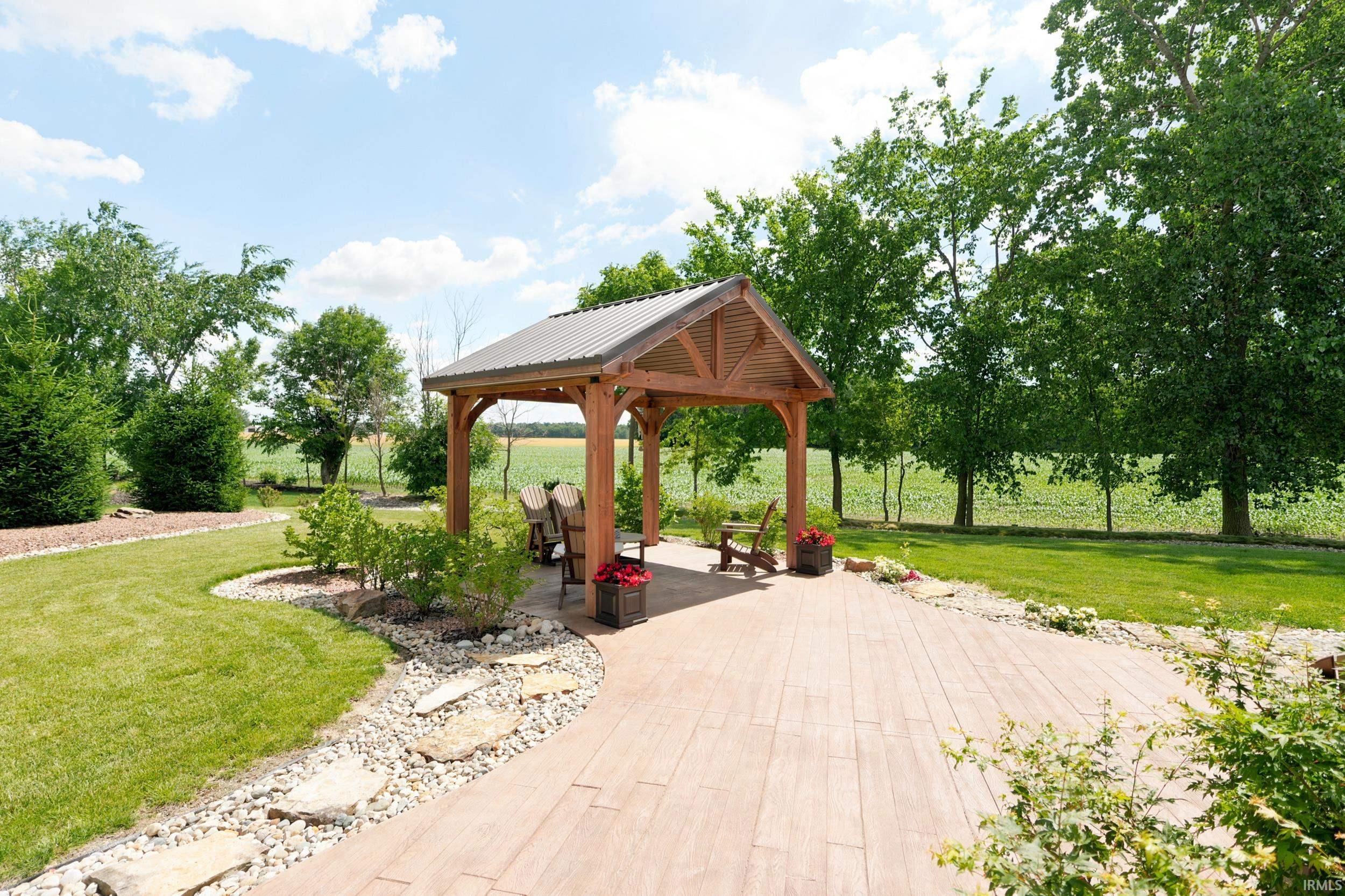 Expansive backyard featuring a wood pergola with metal roof, large stamped concrete patio, manicured lawn, stone pathway with stepping stones, and mature trees bordering the property