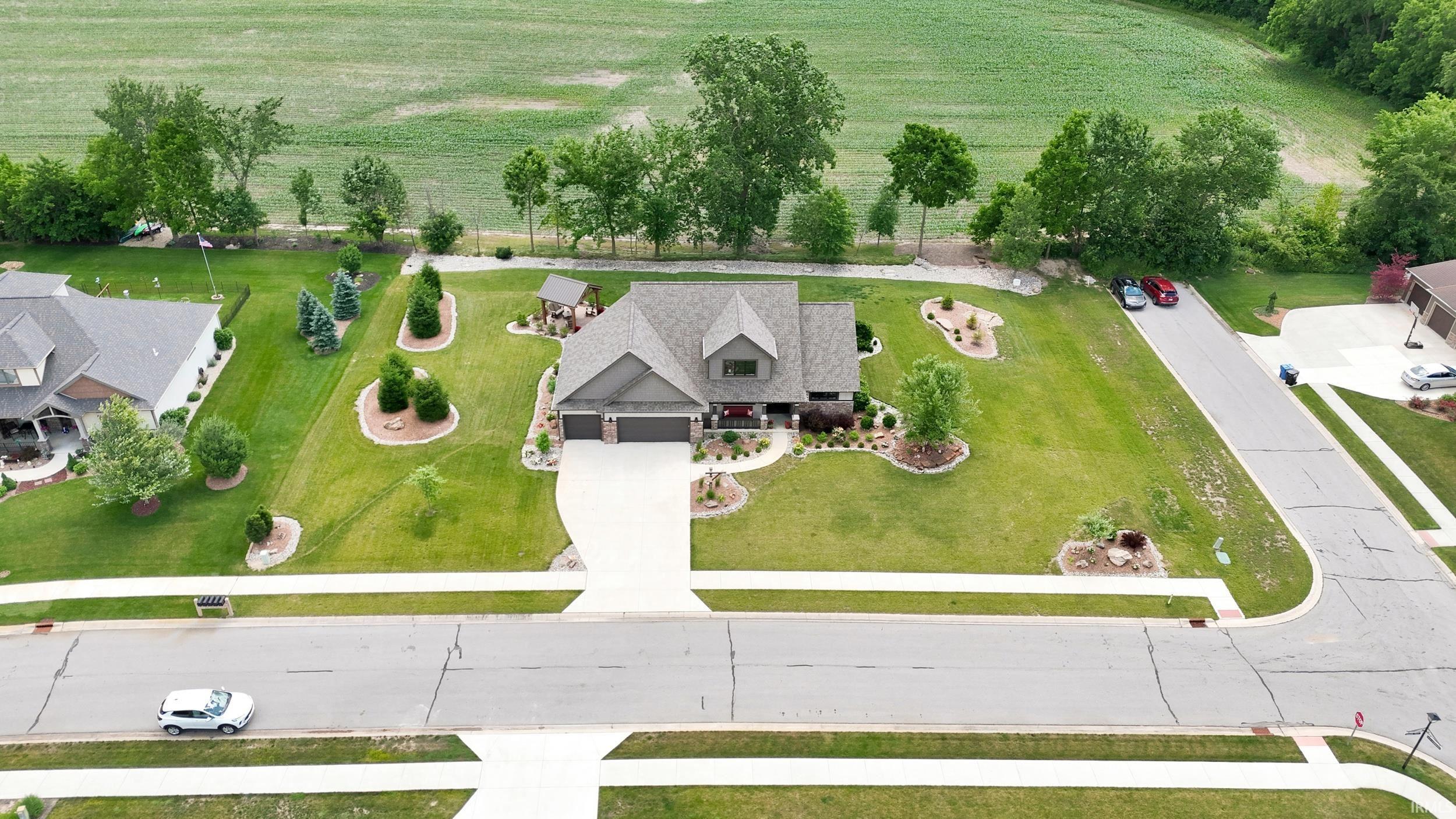 Spacious property featuring a large front yard, mature trees, landscaped beds, an expansive driveway, and a two-car garage