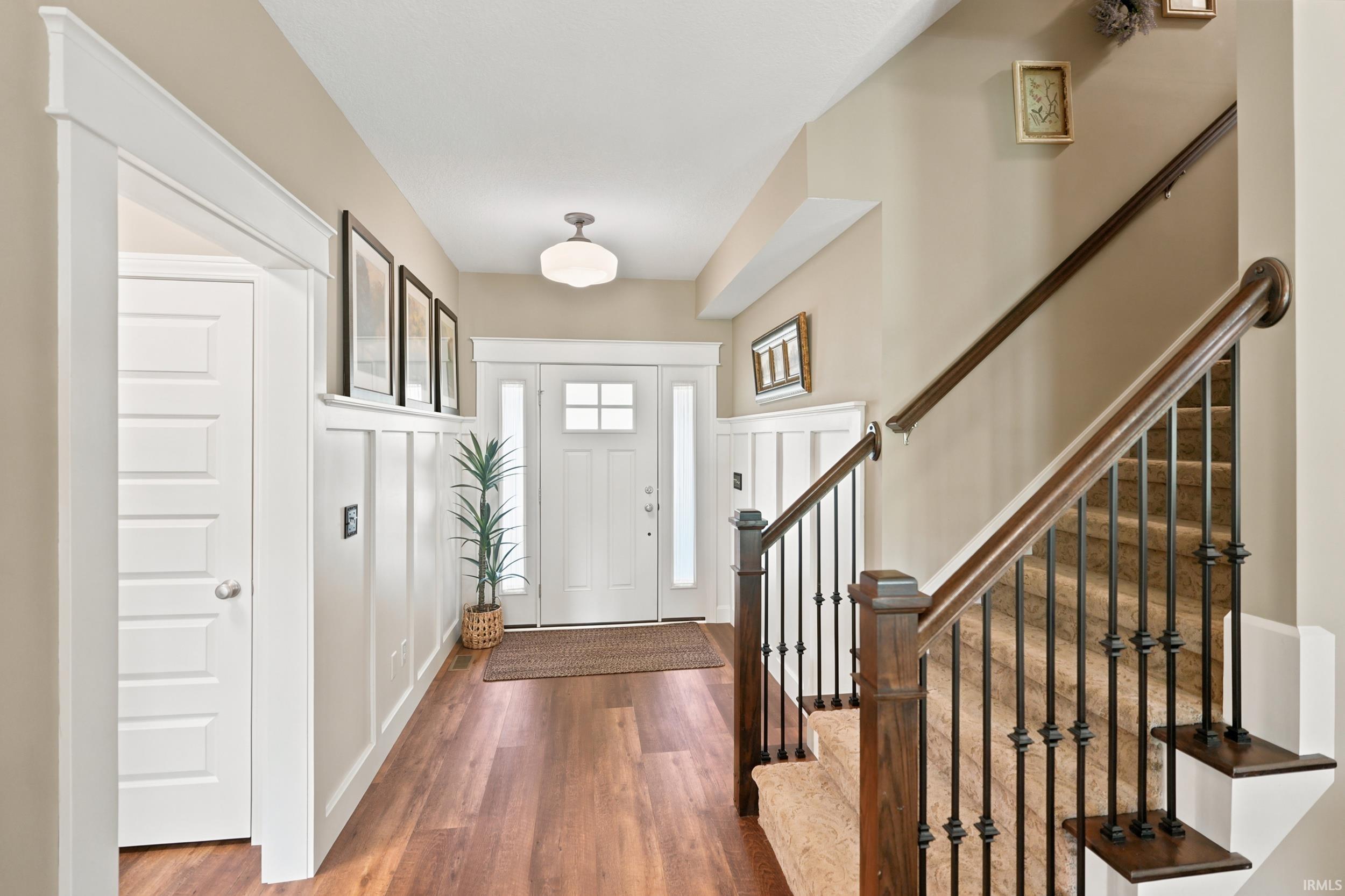 Foyer with wood-finish flooring, white wainscoting, and a paneled entry door with sidelights