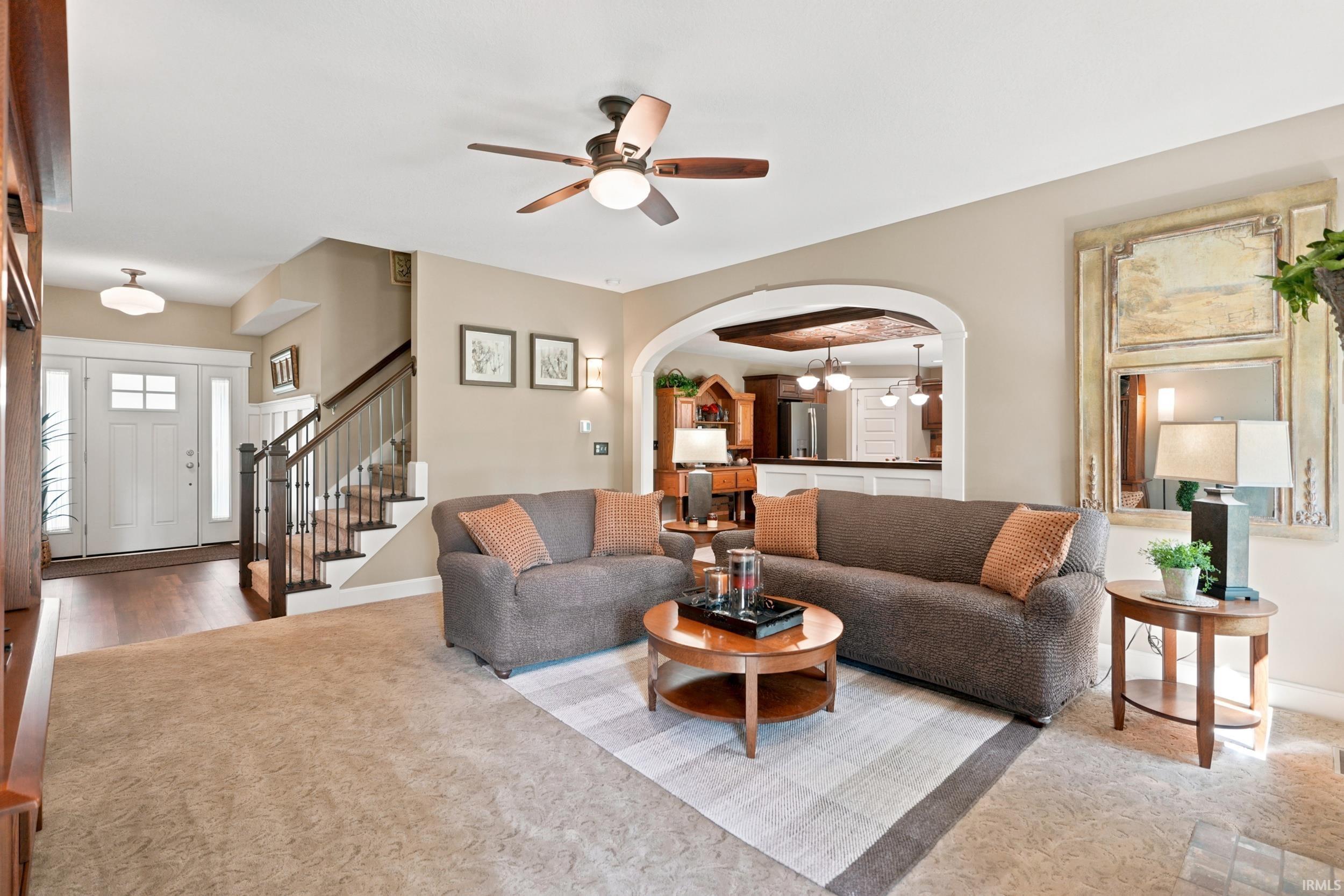 Spacious living area featuring neutral carpeting, a ceiling fan with integrated lighting, and an arched entryway