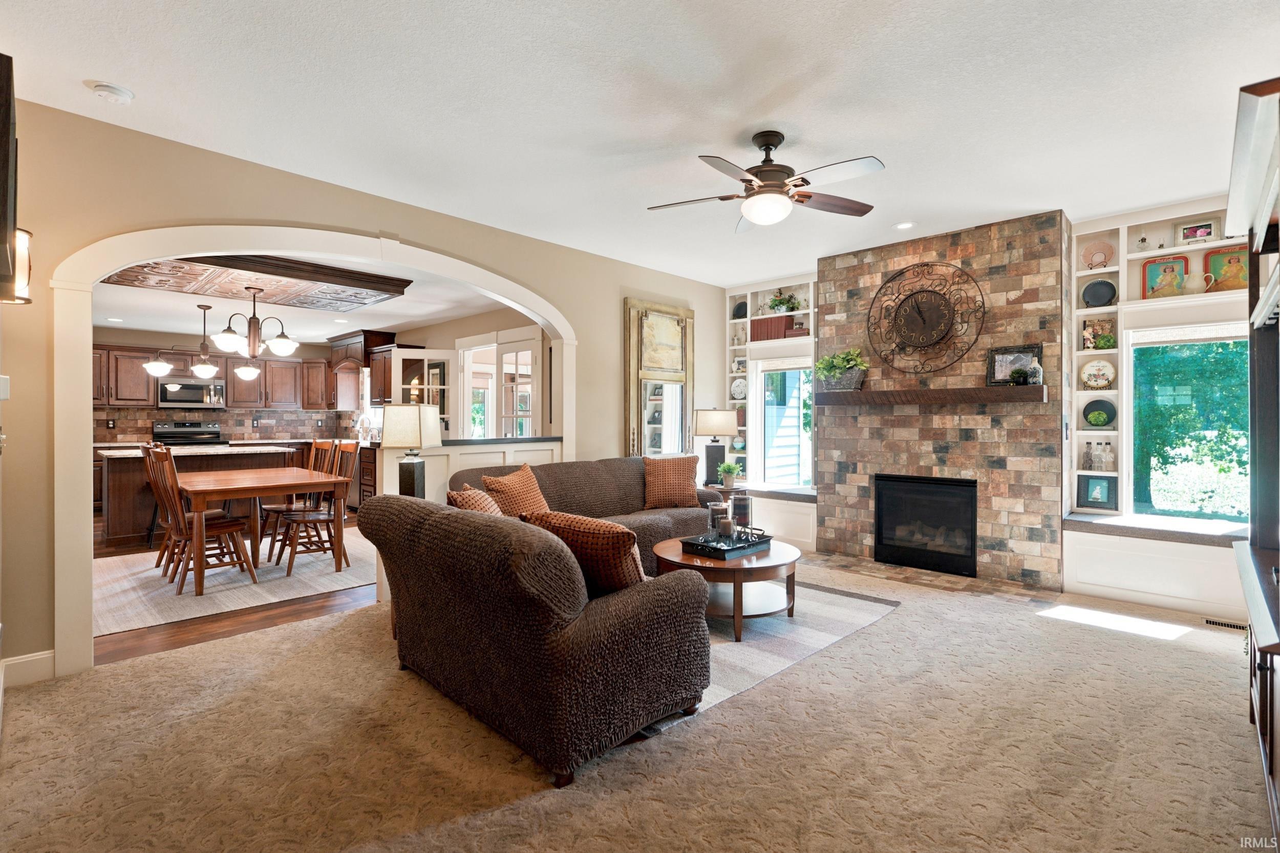Living area featuring a textured carpet, a stone-faced fireplace with a wood mantle, and built-in shelving
