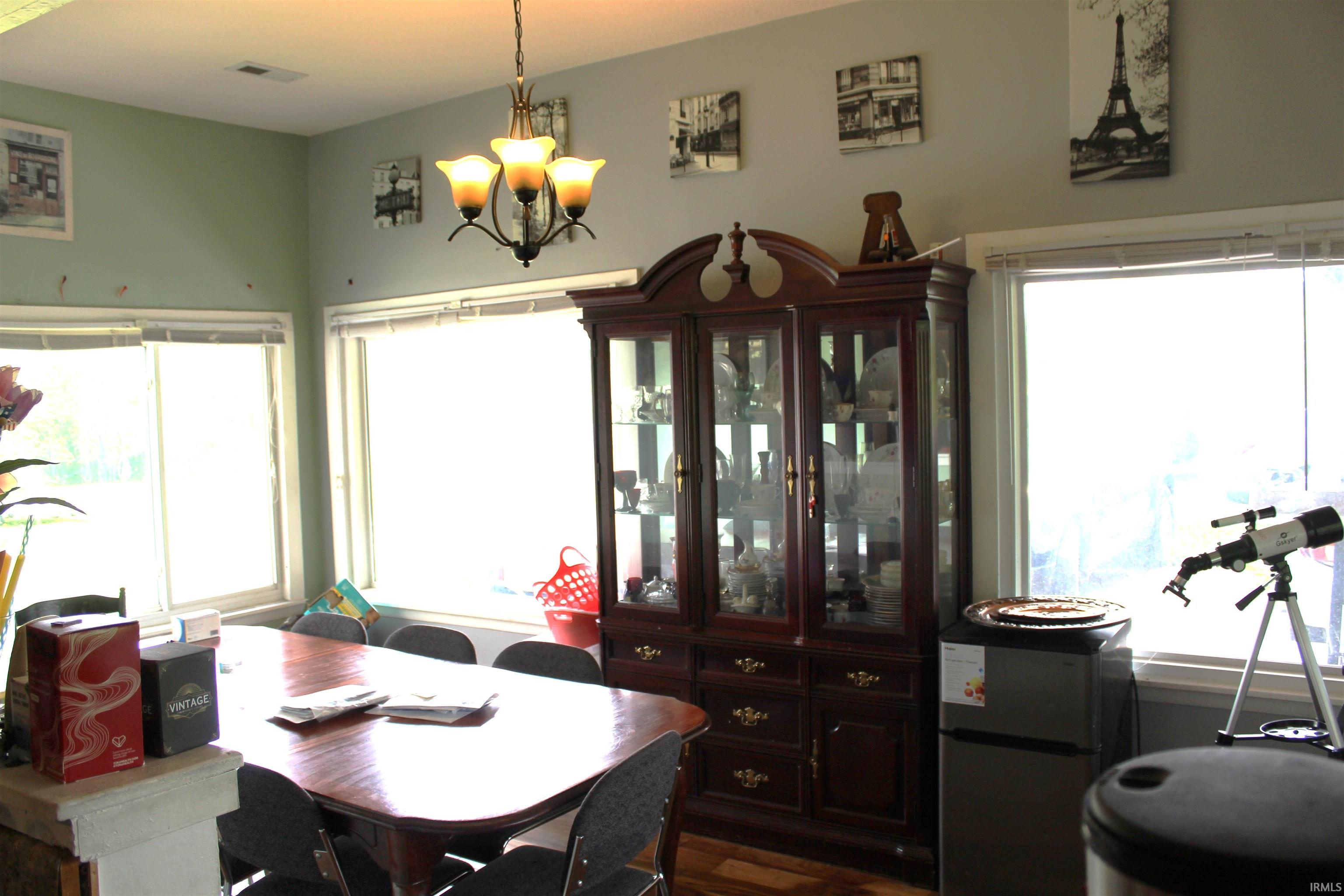 Dining area featuring expansive windows, wood-finish flooring, a chandelier with three frosted glass shades, and light green wall tones