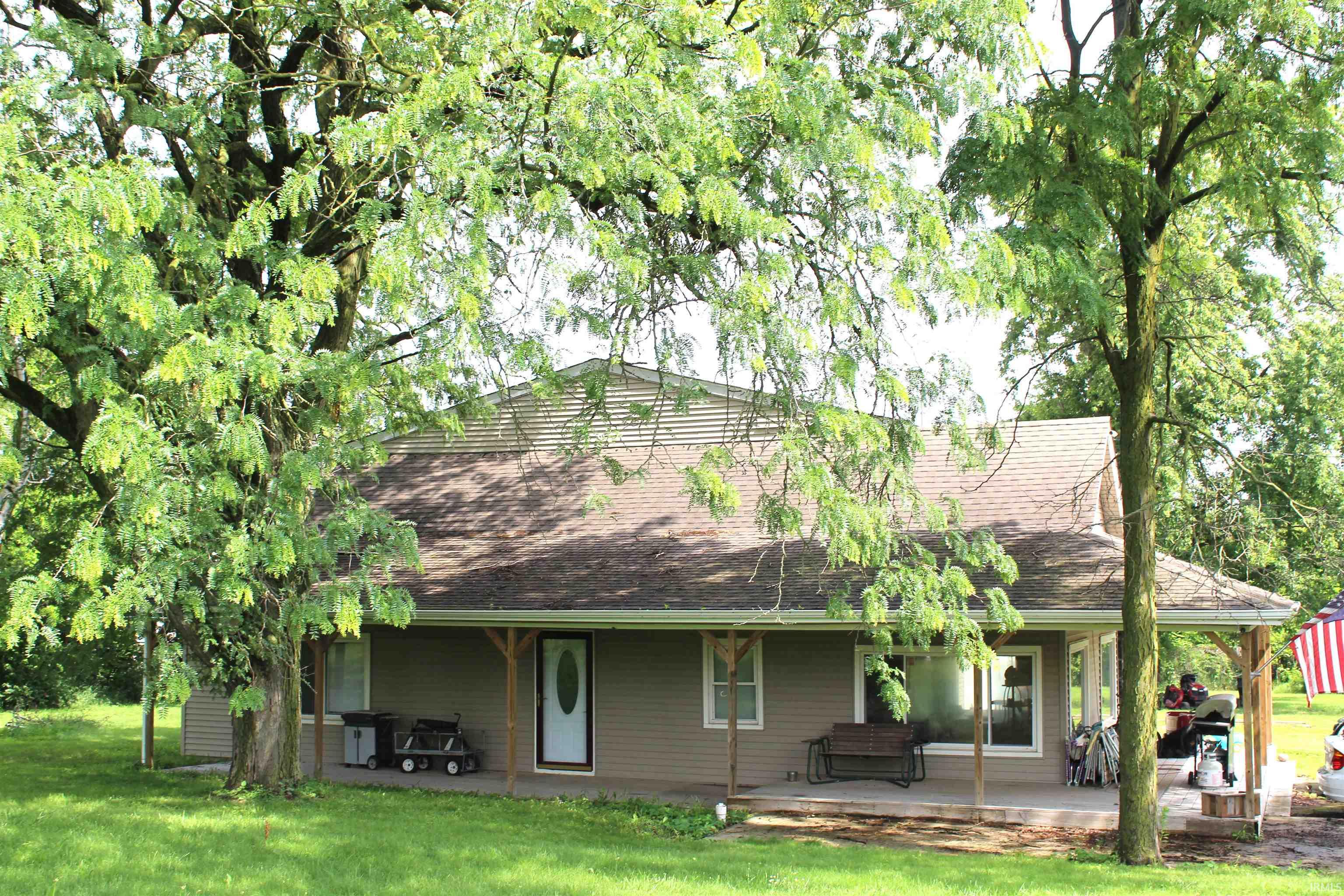 Ranch-style residence featuring a covered front porch, tan siding, and a brown shingle roof