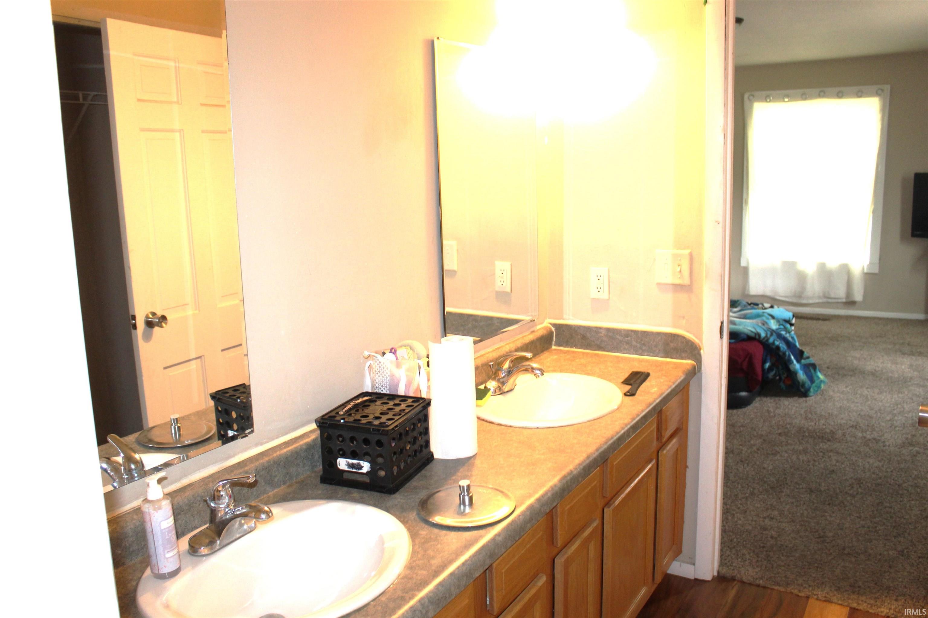 Bathroom vanity featuring dual sinks, laminate countertops, and wood-finish cabinetry
