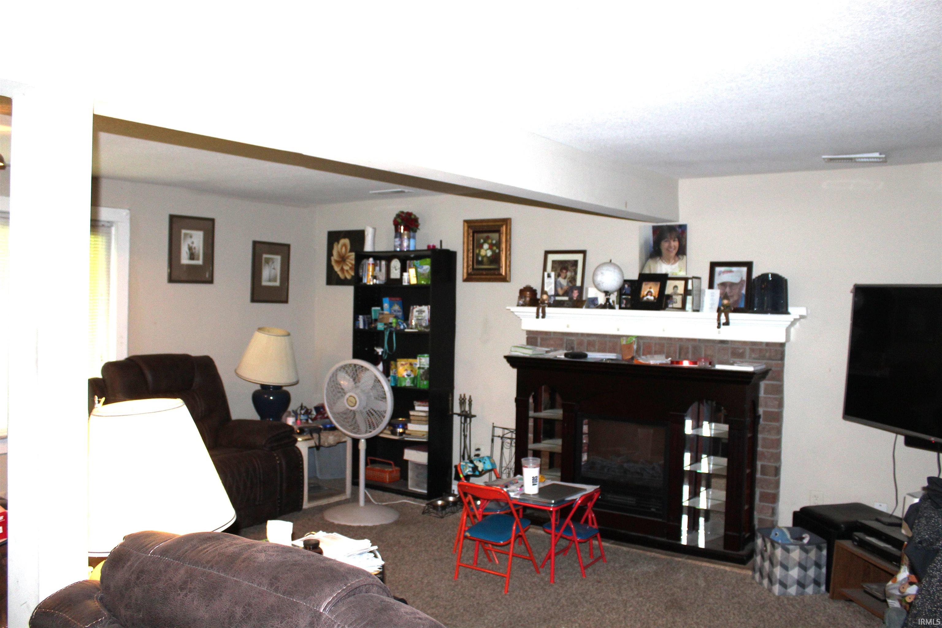 Living area featuring a brick-surround fireplace with a white mantel, light-toned walls, and carpet flooring