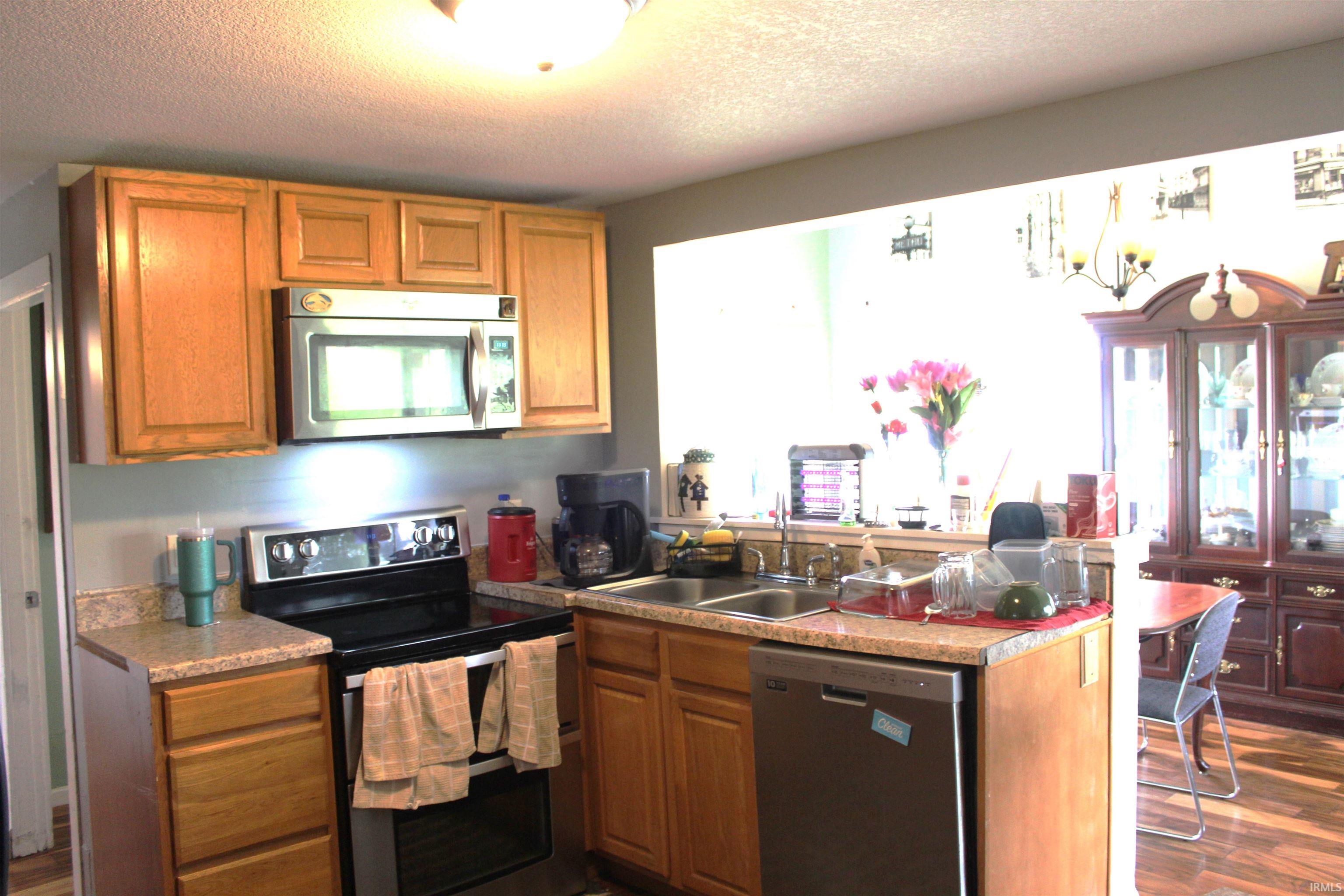 Kitchen featuring light wood cabinetry, stone-look countertops, and stainless steel appliances including an over-range microwave, electric range, and dishwasher
