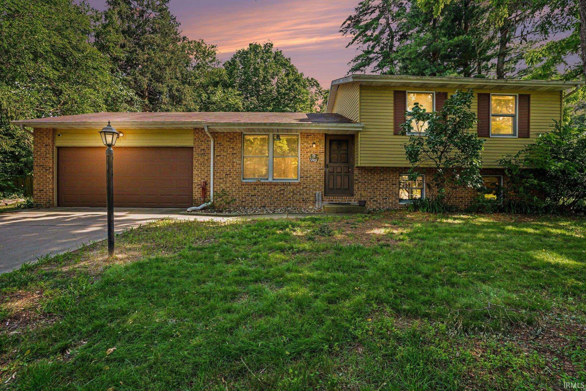 Split-level residence featuring a brick and siding exterior, an attached two-car garage with a brown door, and a paved driveway