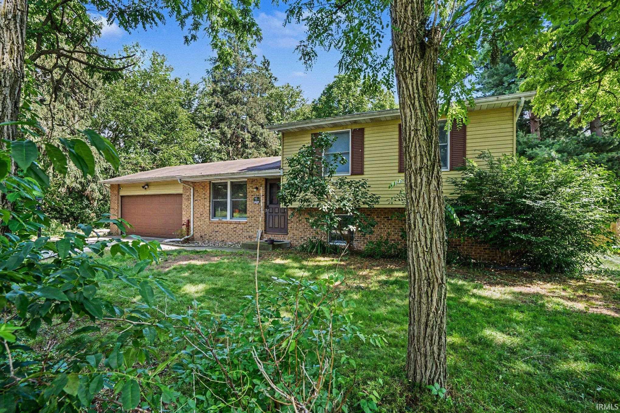Split-level residence featuring a brick and yellow siding exterior, an attached garage with a brown door, and prominent mature trees