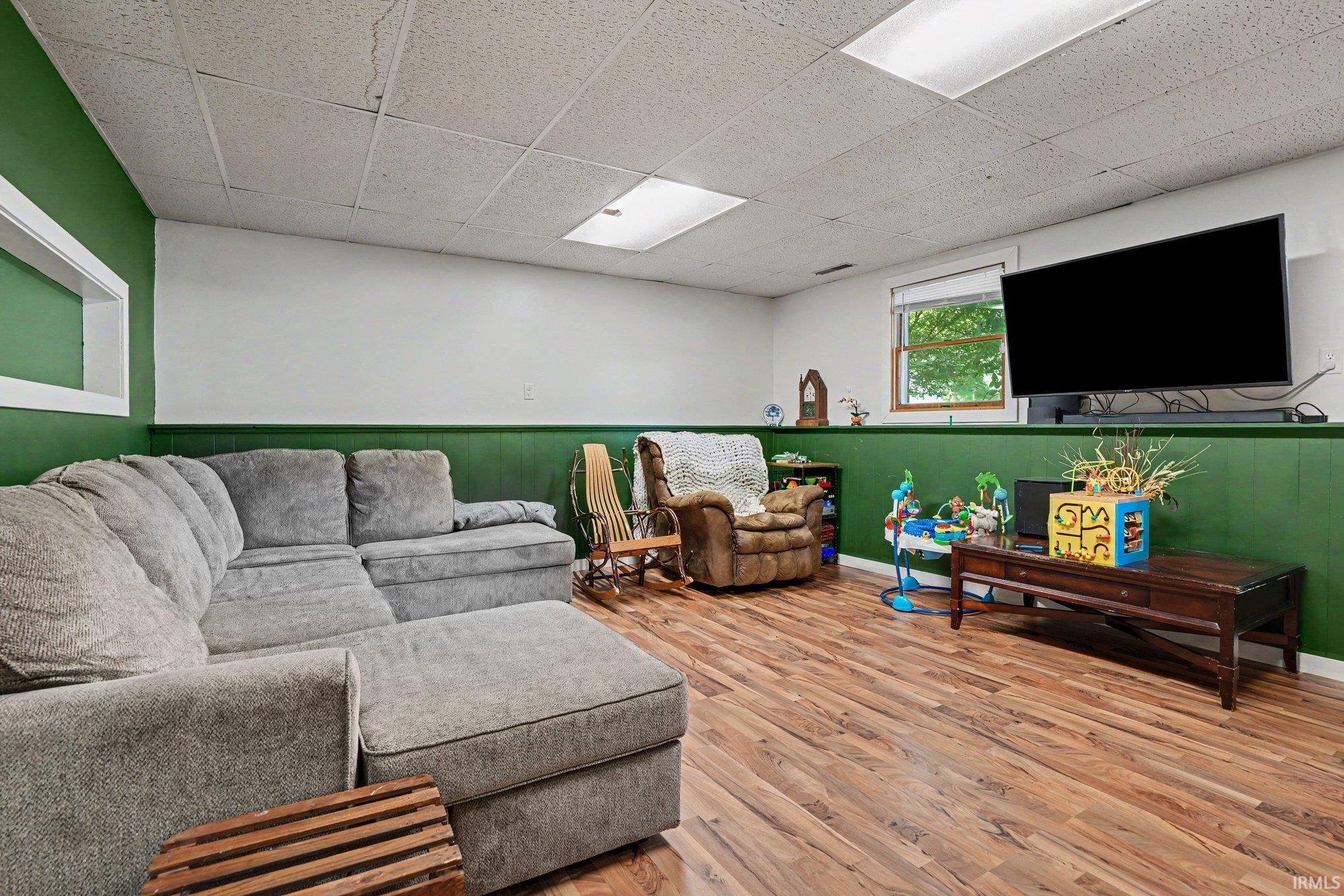Recreation area featuring wood-finish flooring, drop ceiling with integrated lighting, and a window providing natural light