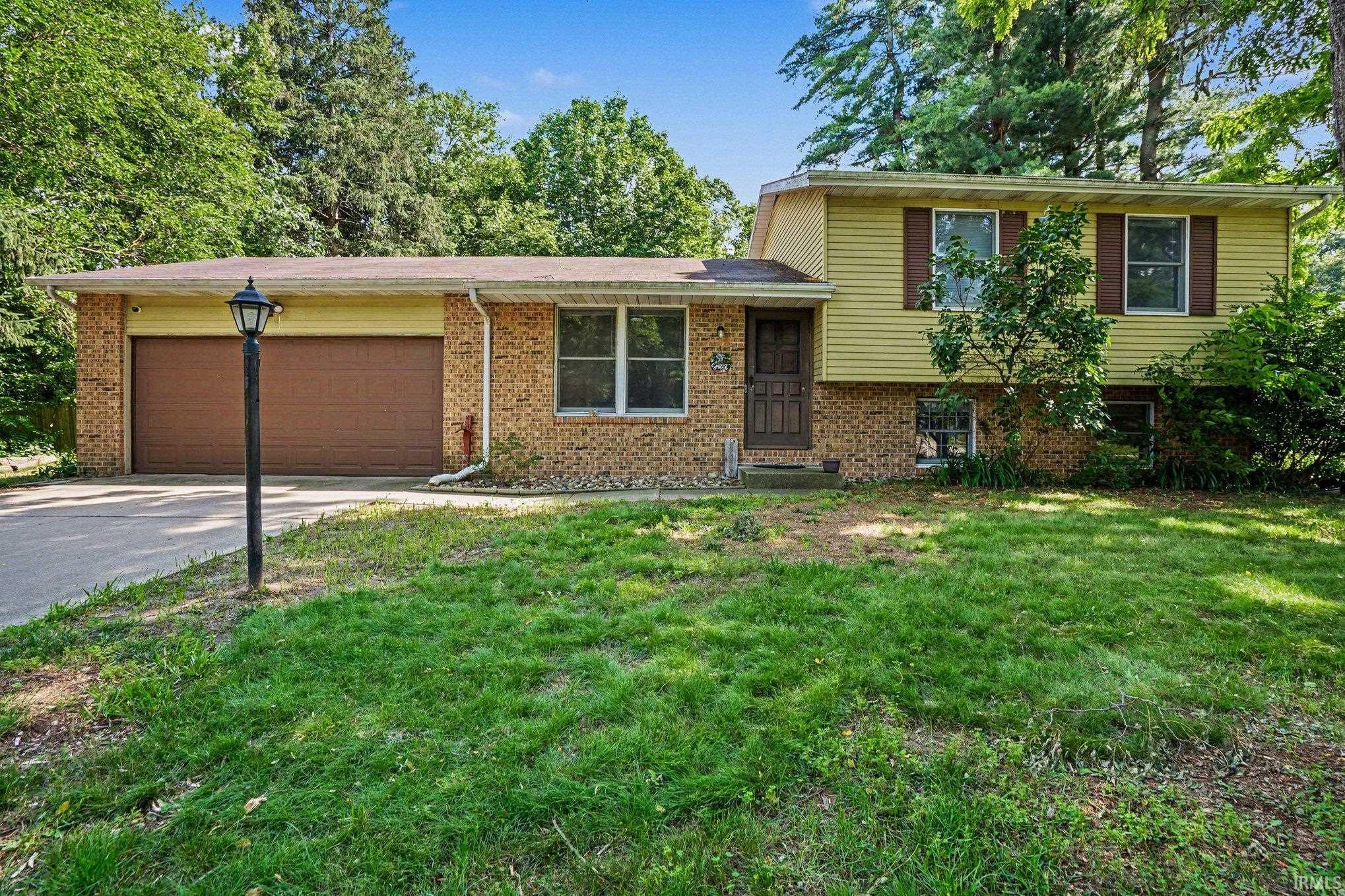 Split-level residence featuring a brick and siding exterior, an attached two-car garage with brown doors, and a paved driveway