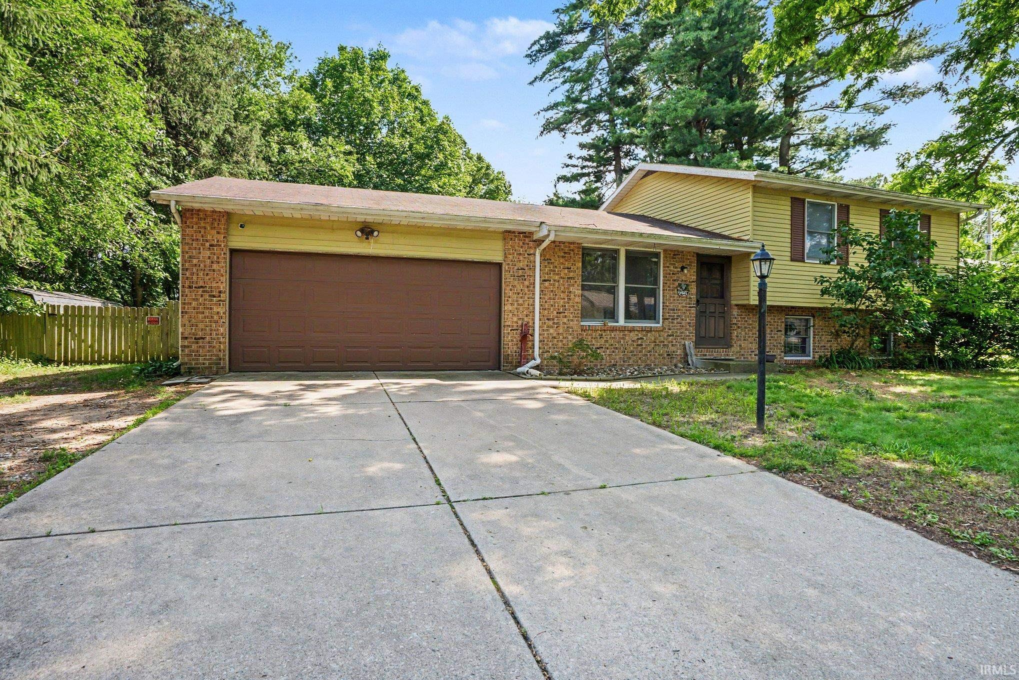 Split-level home featuring a concrete driveway, an attached two-car garage with a brown door, and a brick facade