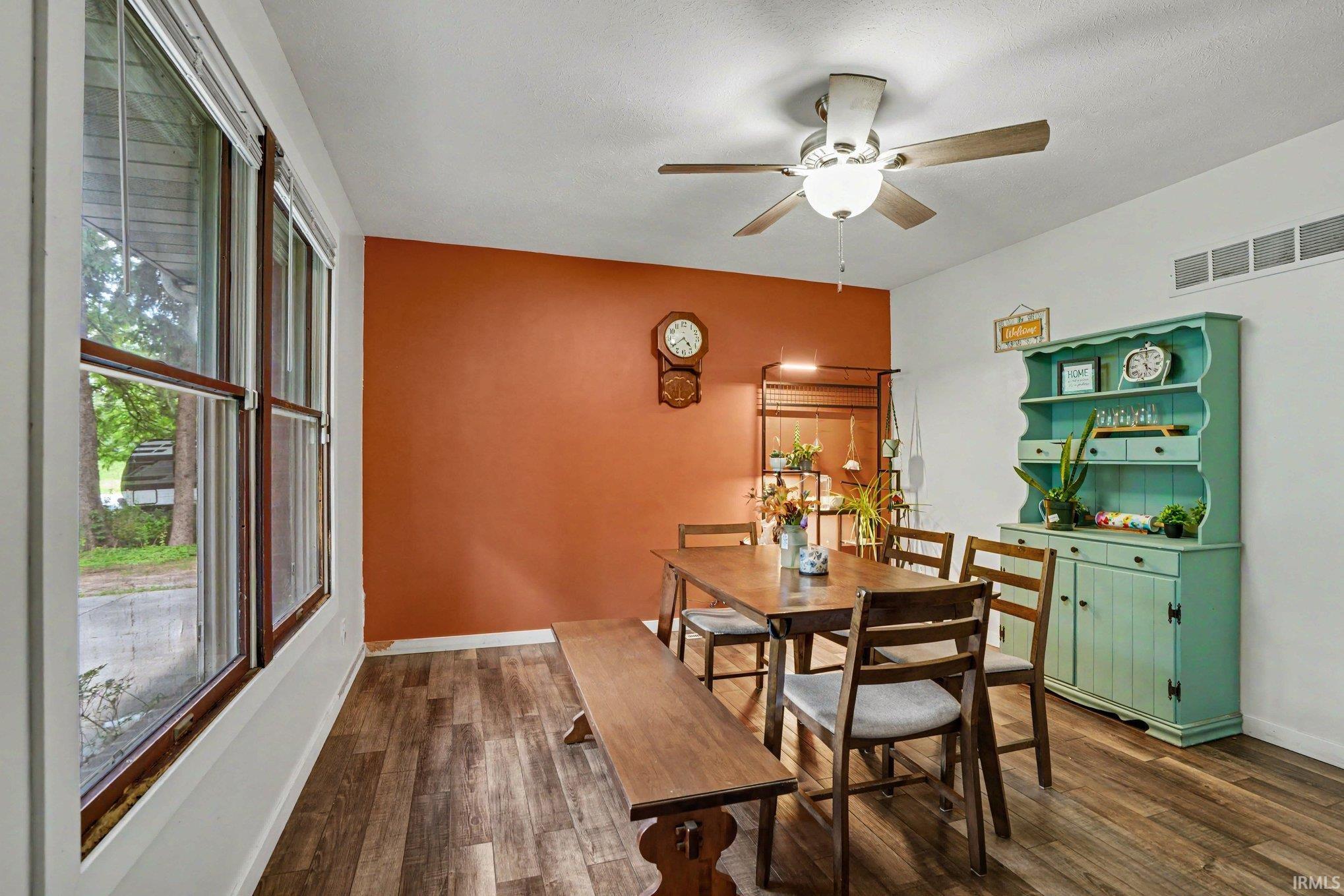 Spacious dining area featuring wood-finish flooring, a ceiling fan with integrated lighting, and a prominent accent wall