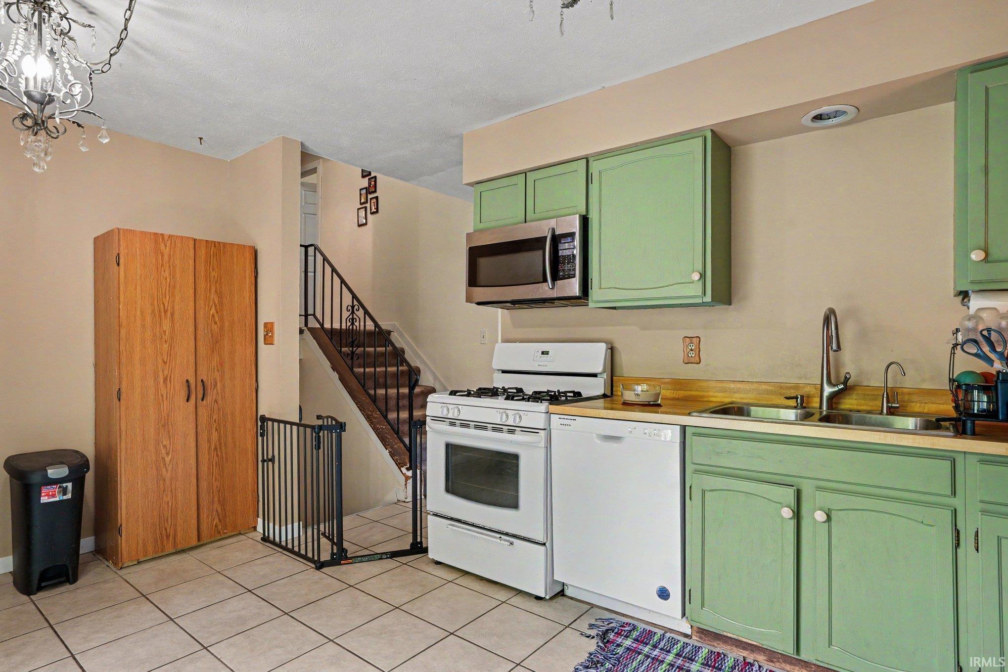 Kitchen featuring white appliances, green cabinetry, a double basin sink, and tile flooring
