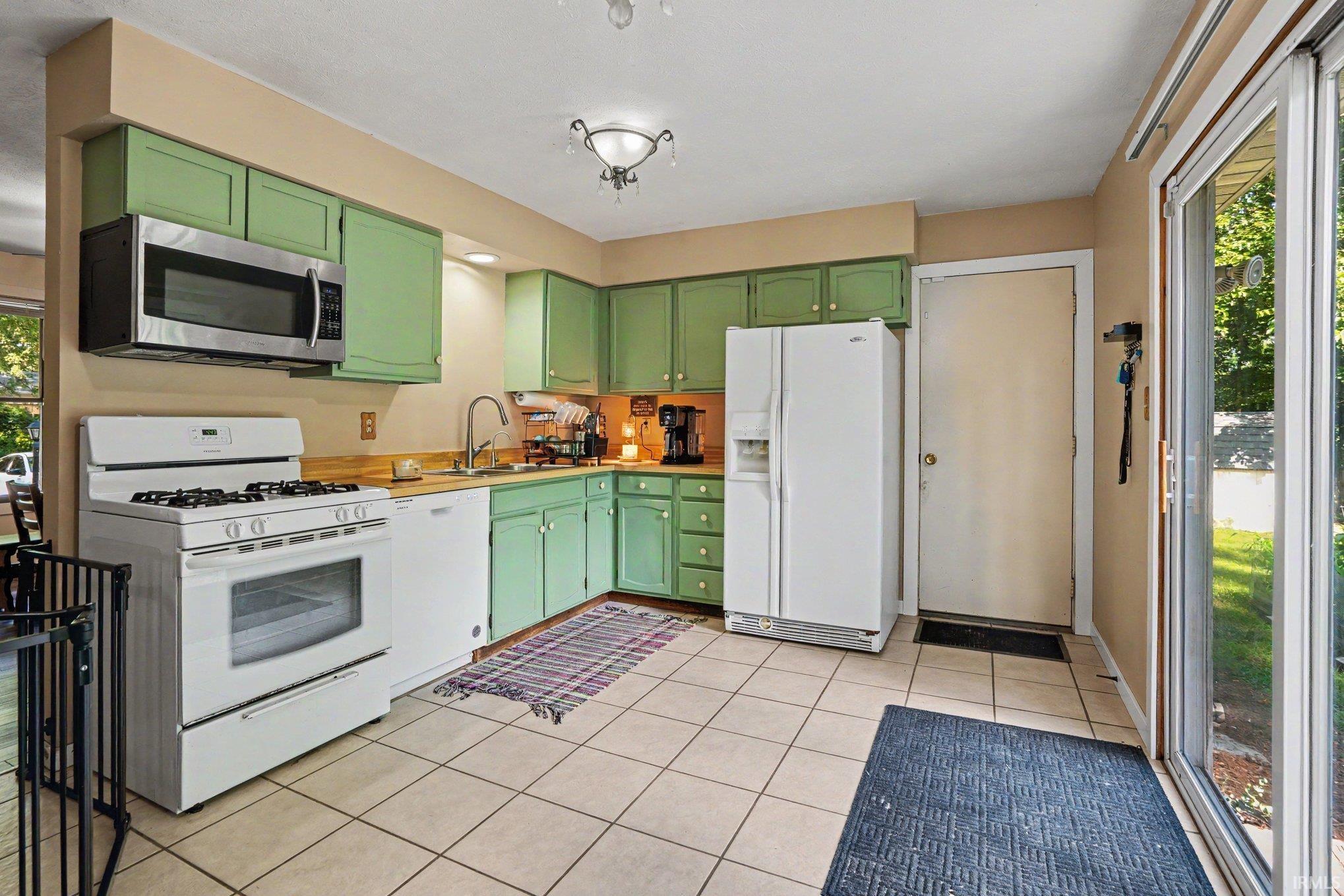 Kitchen featuring green cabinetry, tile flooring, a stainless steel microwave, a white gas range, and a white side-by-side refrigerator