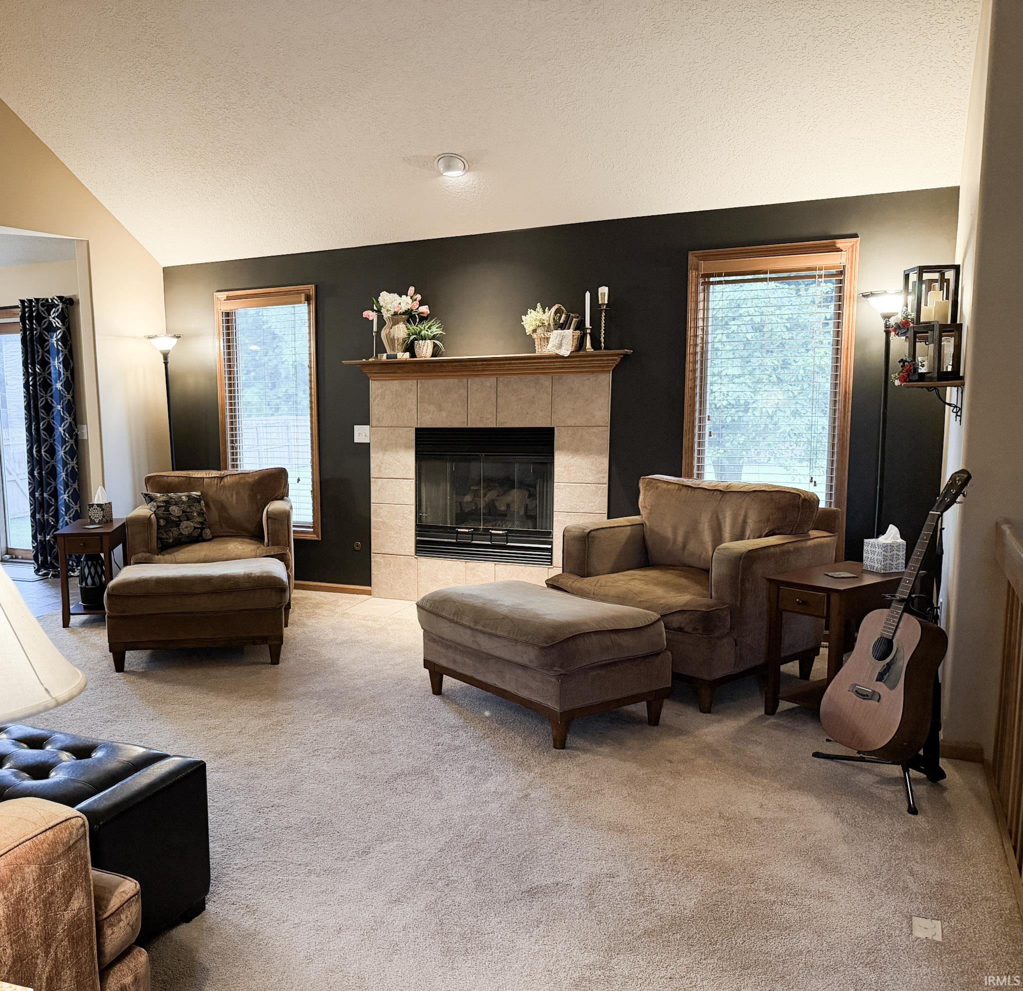 Living area featuring a tiled fireplace with a wood mantle, vaulted ceiling, and recessed lighting