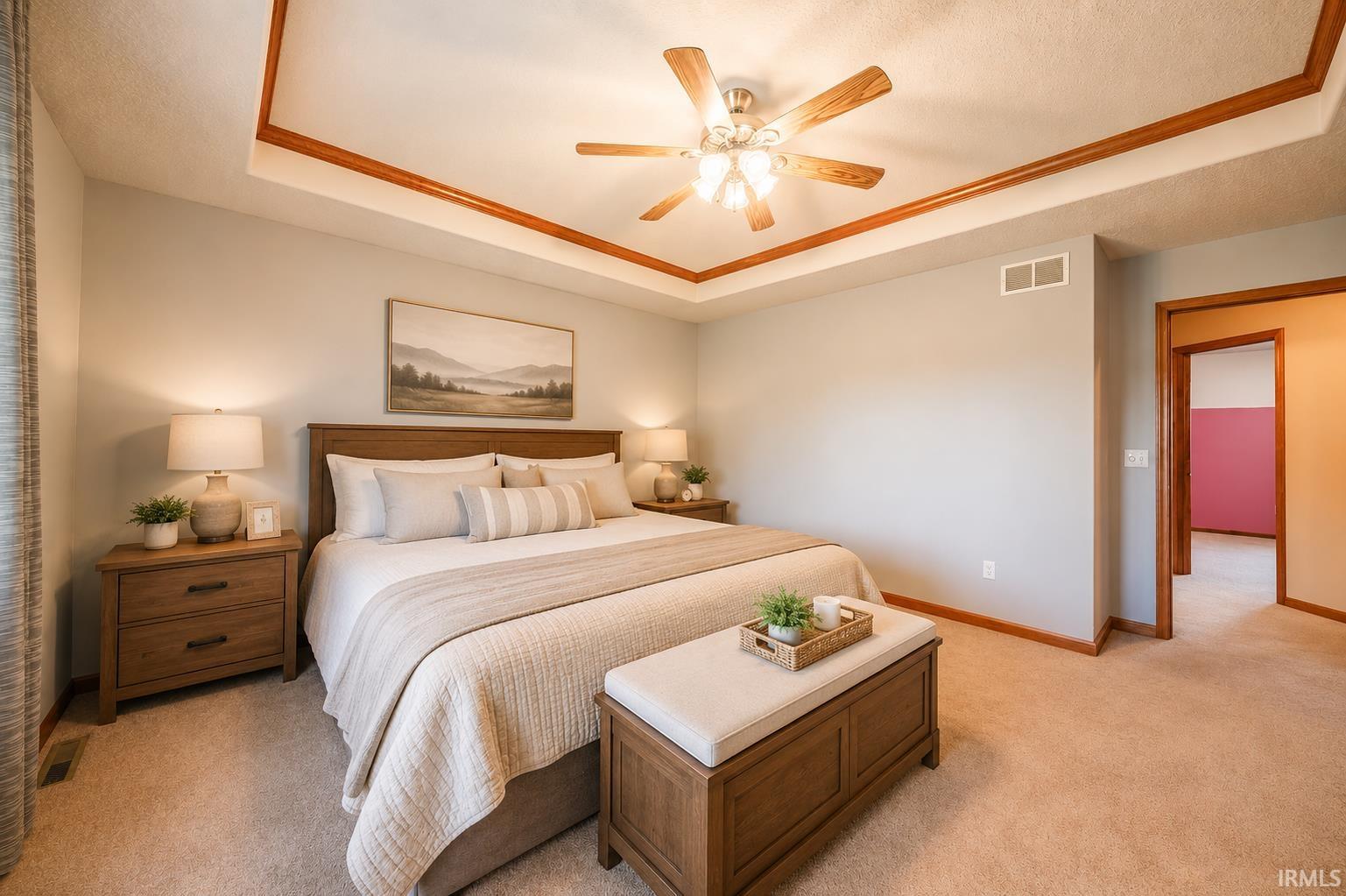 Carpeted bedroom with a tray ceiling featuring wood trim and a ceiling fan