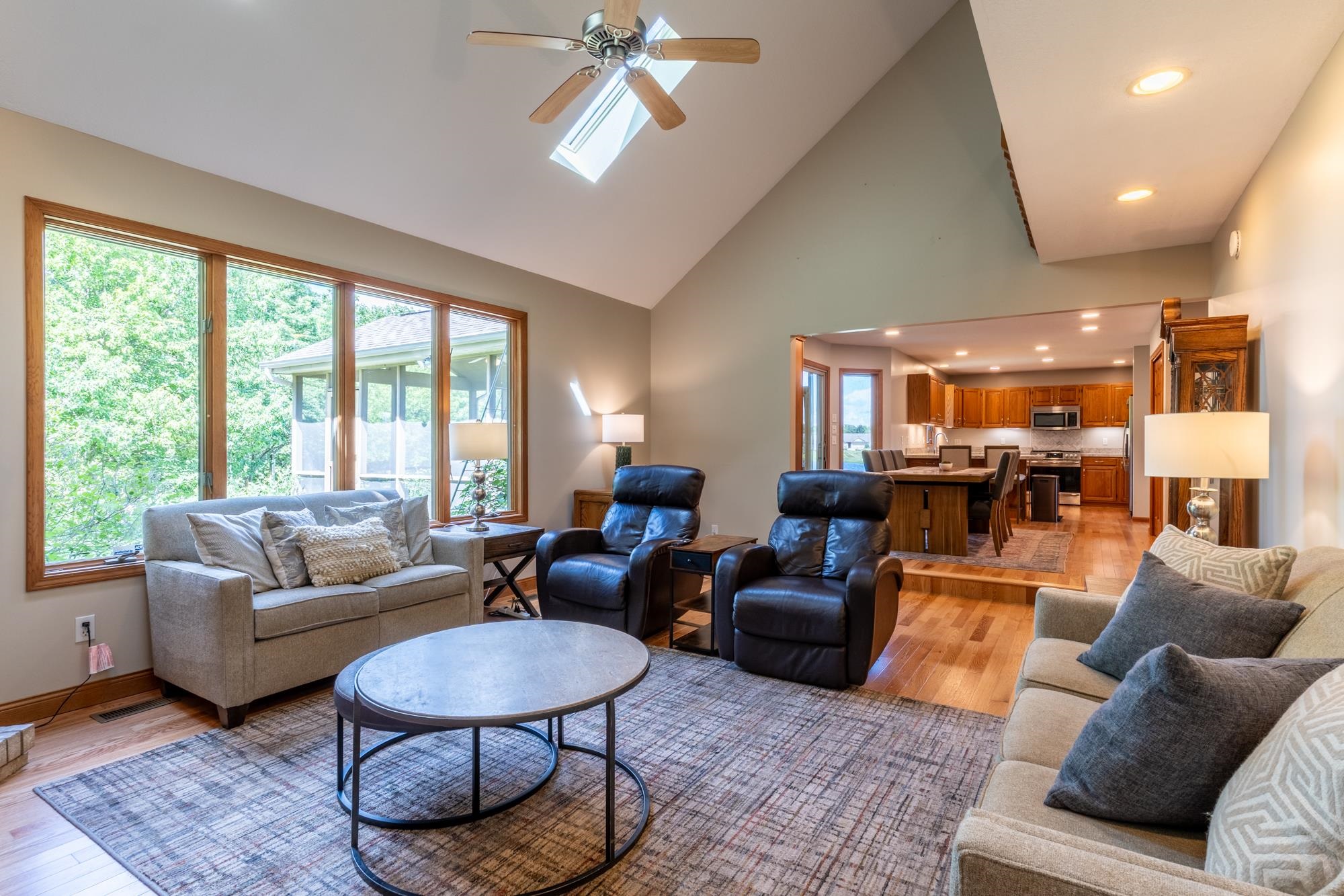Vaulted ceiling living area featuring multiple large windows, wood-finish flooring, and recessed lighting