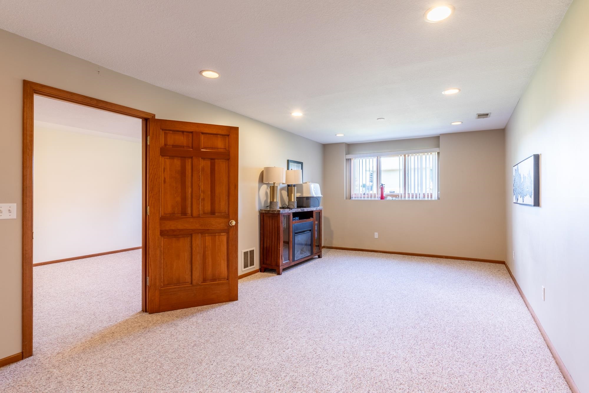 Spacious room featuring light-toned carpeting, recessed ceiling lighting, and a window with horizontal blinds