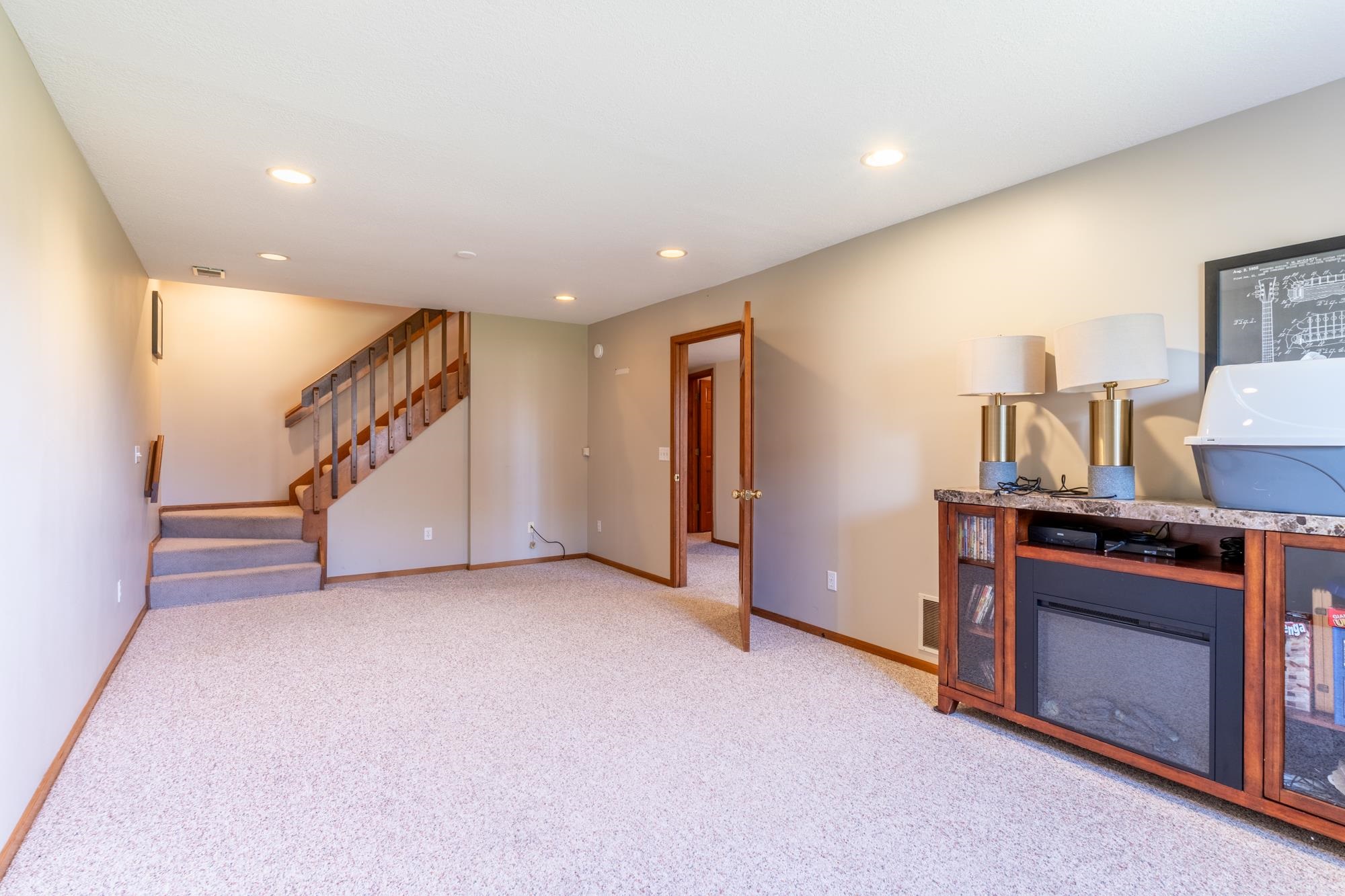 Spacious carpeted room featuring recessed lighting and a wood staircase with carpeted treads