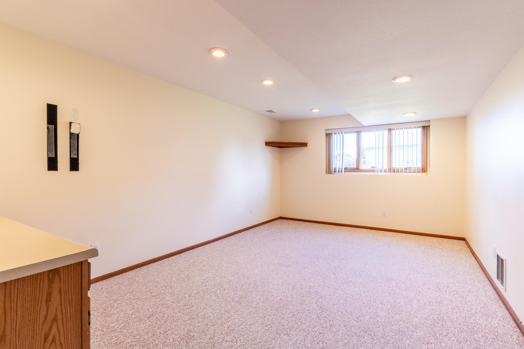 Carpeted room featuring a window with vertical blinds, recessed lighting, and a built-in wooden shelf