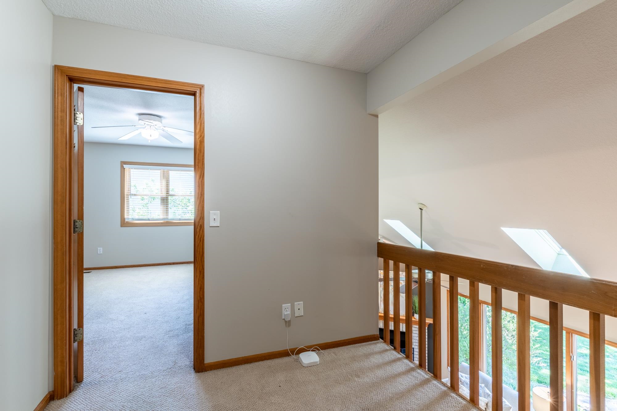 Upper-level landing with carpeting and wood railing, providing an open view to the lower level