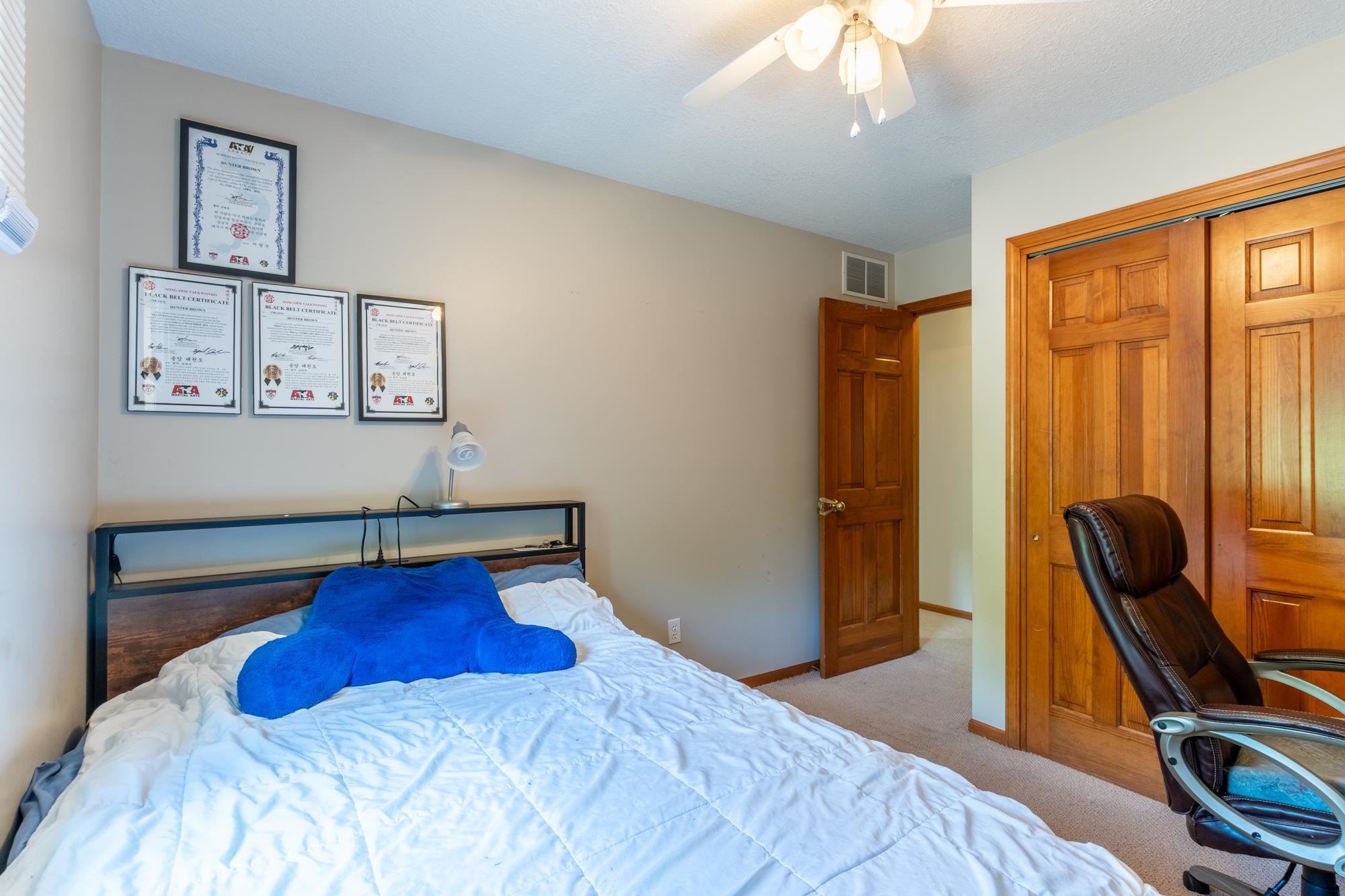 Carpeted room featuring a ceiling fan with light fixture, natural wood-finish doors, and neutral wall paint