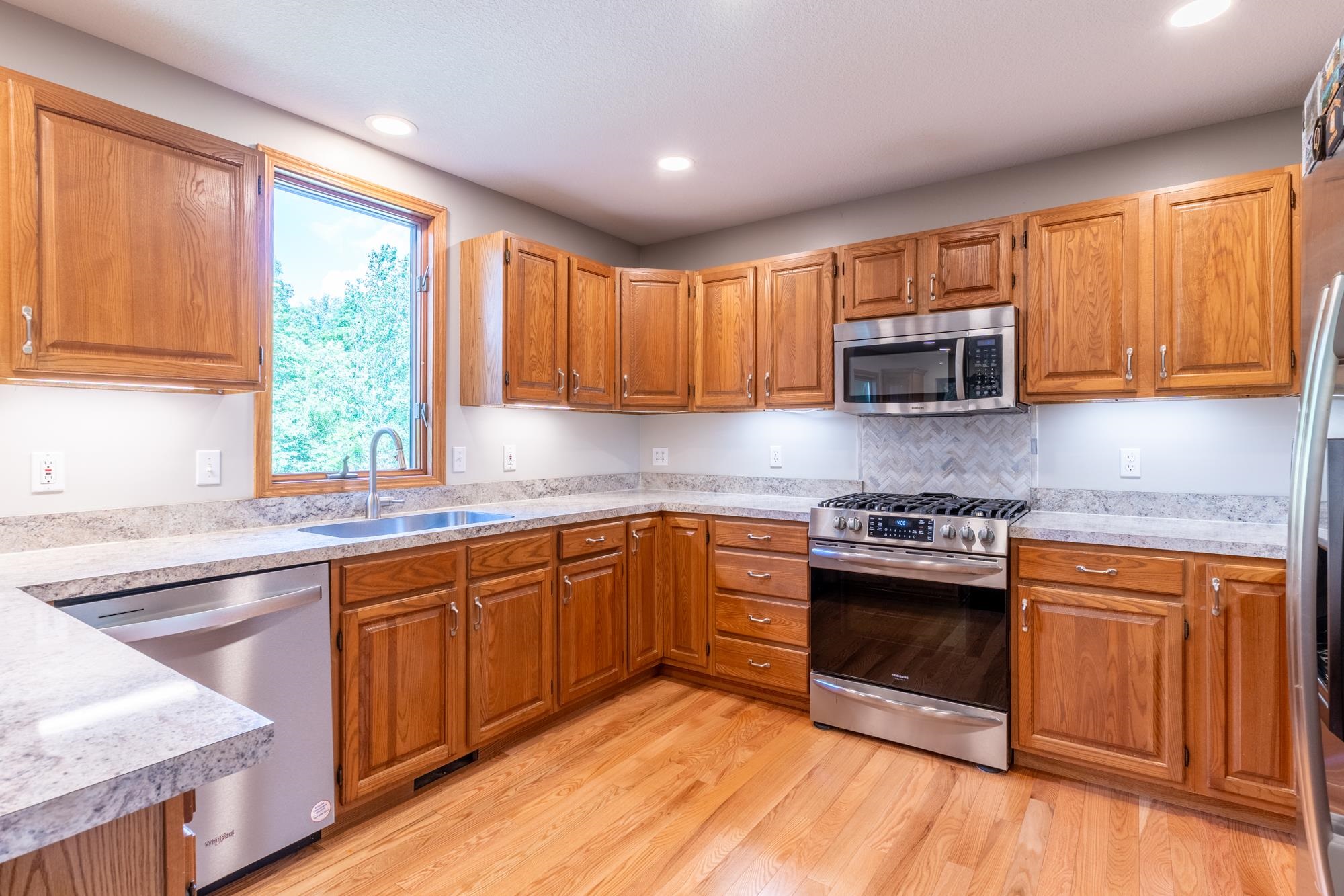 Kitchen featuring wood cabinetry, light-toned countertops, stainless steel appliances, and a tiled backsplash