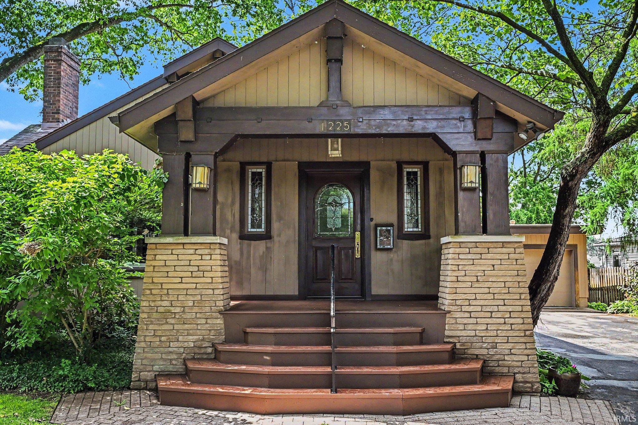 Craftsman-style facade featuring a prominent porch with stout columns, a dark wood entry door with leaded glass, and flanking vertical windows