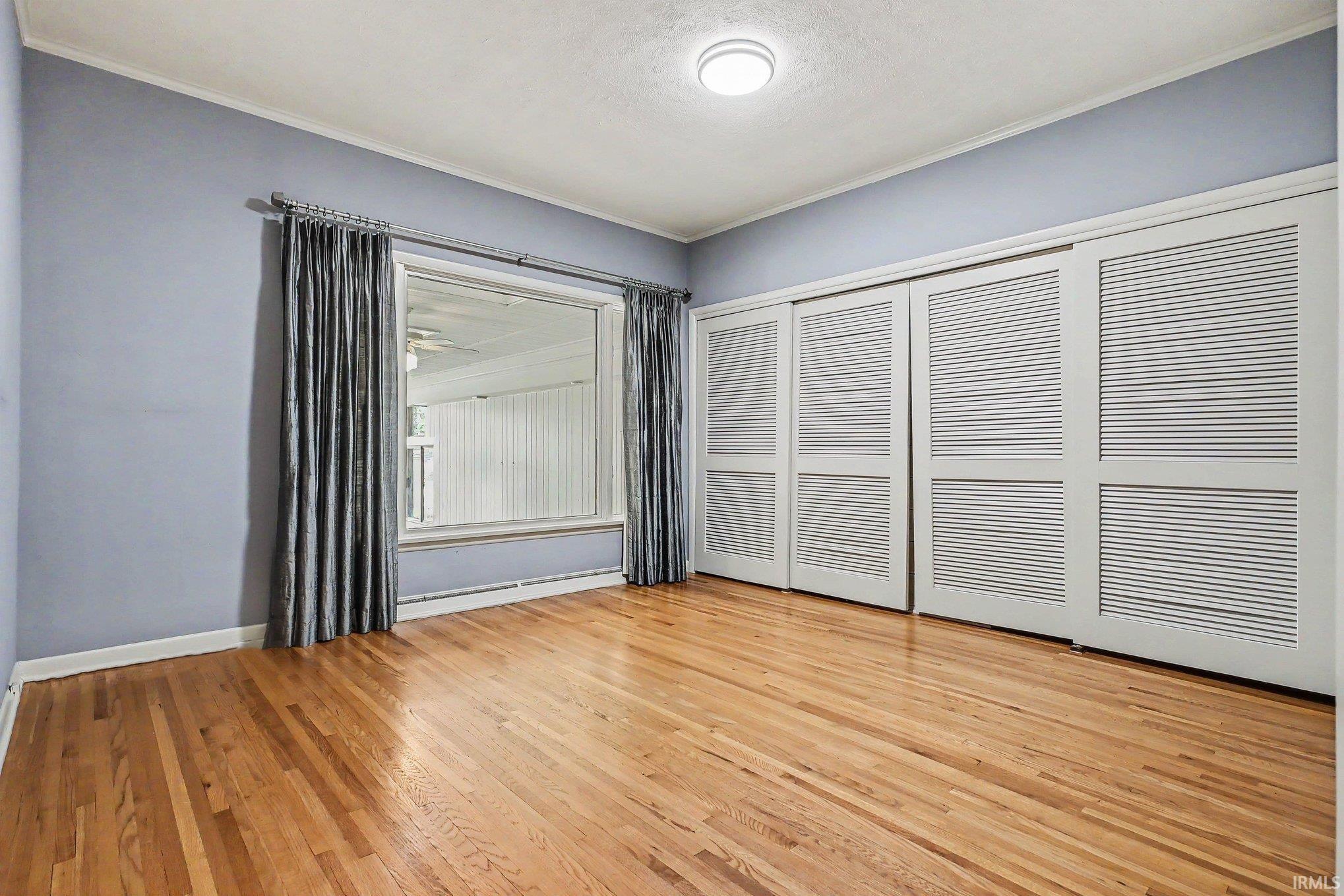 Hardwood flooring in a room featuring a large window, white trim, and a full wall of sliding closet doors