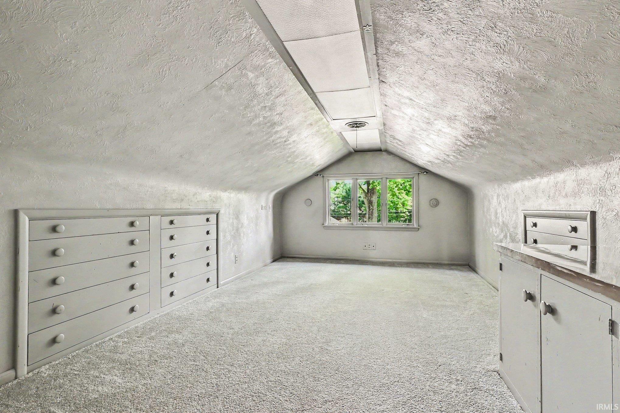 Carpeted attic bedroom with built in cabinetry, sloped ceilings and a gabled window