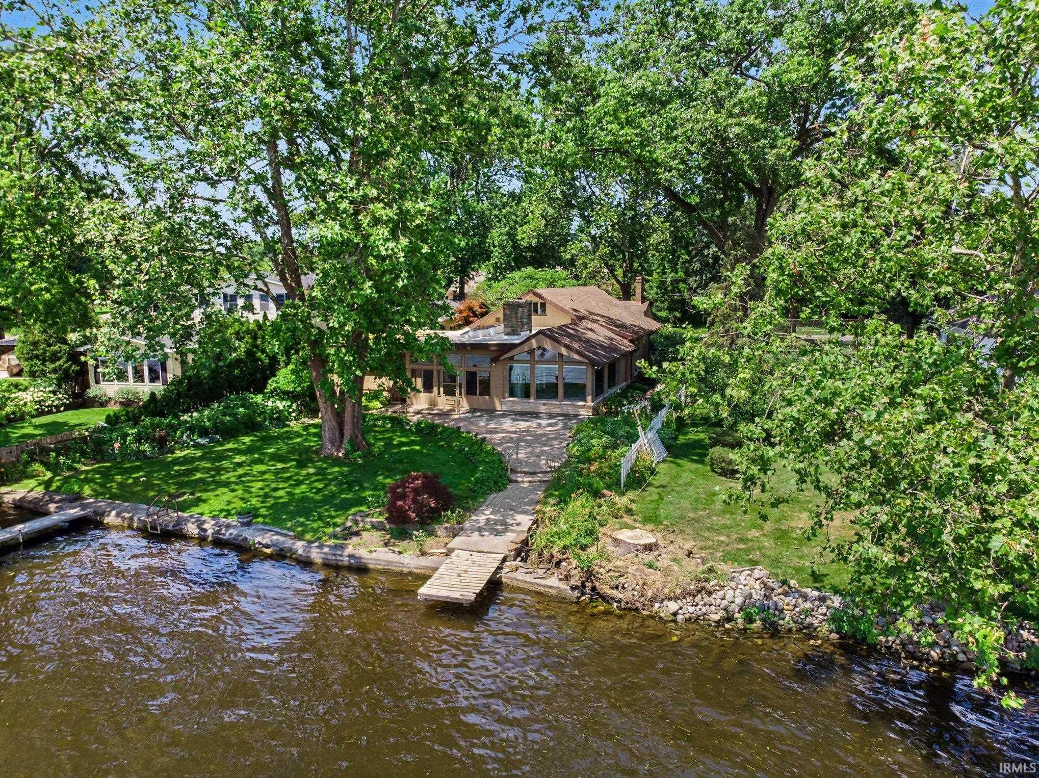 Waterfront property featuring a private dock and pier, expansive green lawn, mature trees, and patio