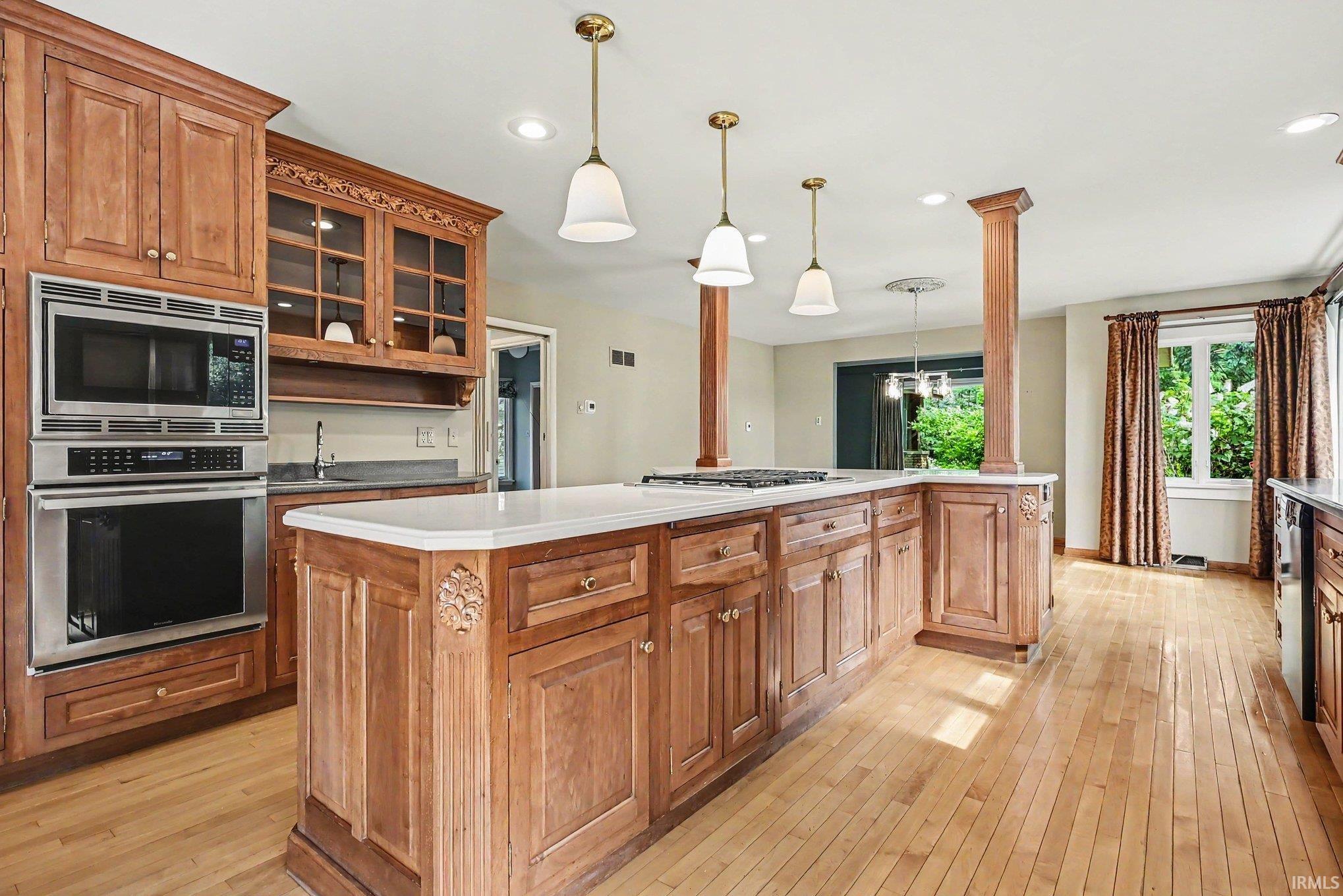 Kitchen featuring light wood cabinetry, stainless steel double oven, large center island with stovetop, light wood-finish flooring, and recessed lighting