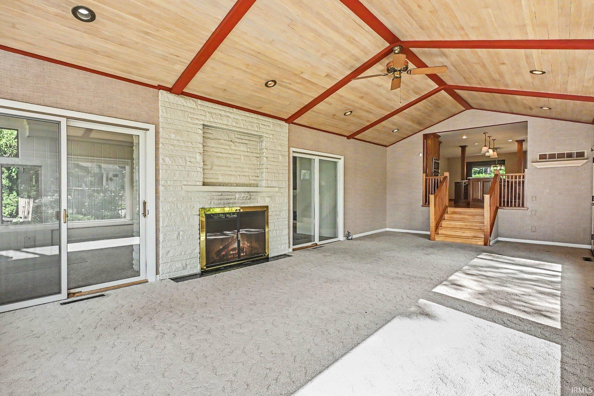 Spacious room featuring a vaulted wood-paneled ceiling with exposed beams, a white brick fireplace, and sliding glass doors