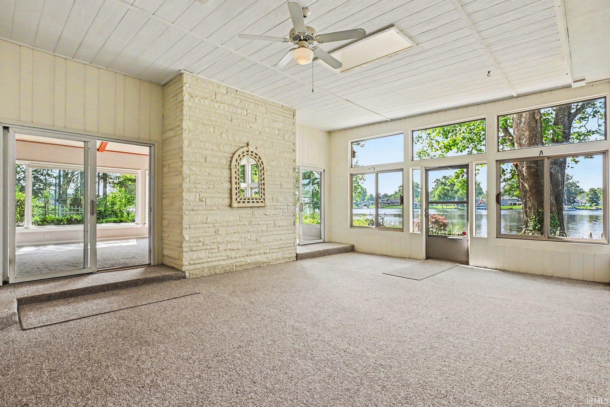 Sunroom featuring expansive windows with water views, a ceiling fan, and sliding glass doors opening to an outdoor patio